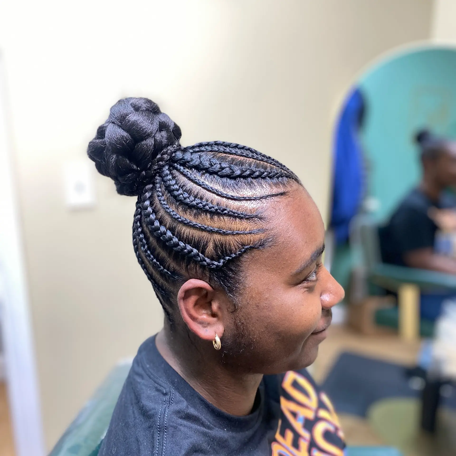 A neat protective hairstyle featuring curved cornrows directed upward into a sculptural high braided bun. 1