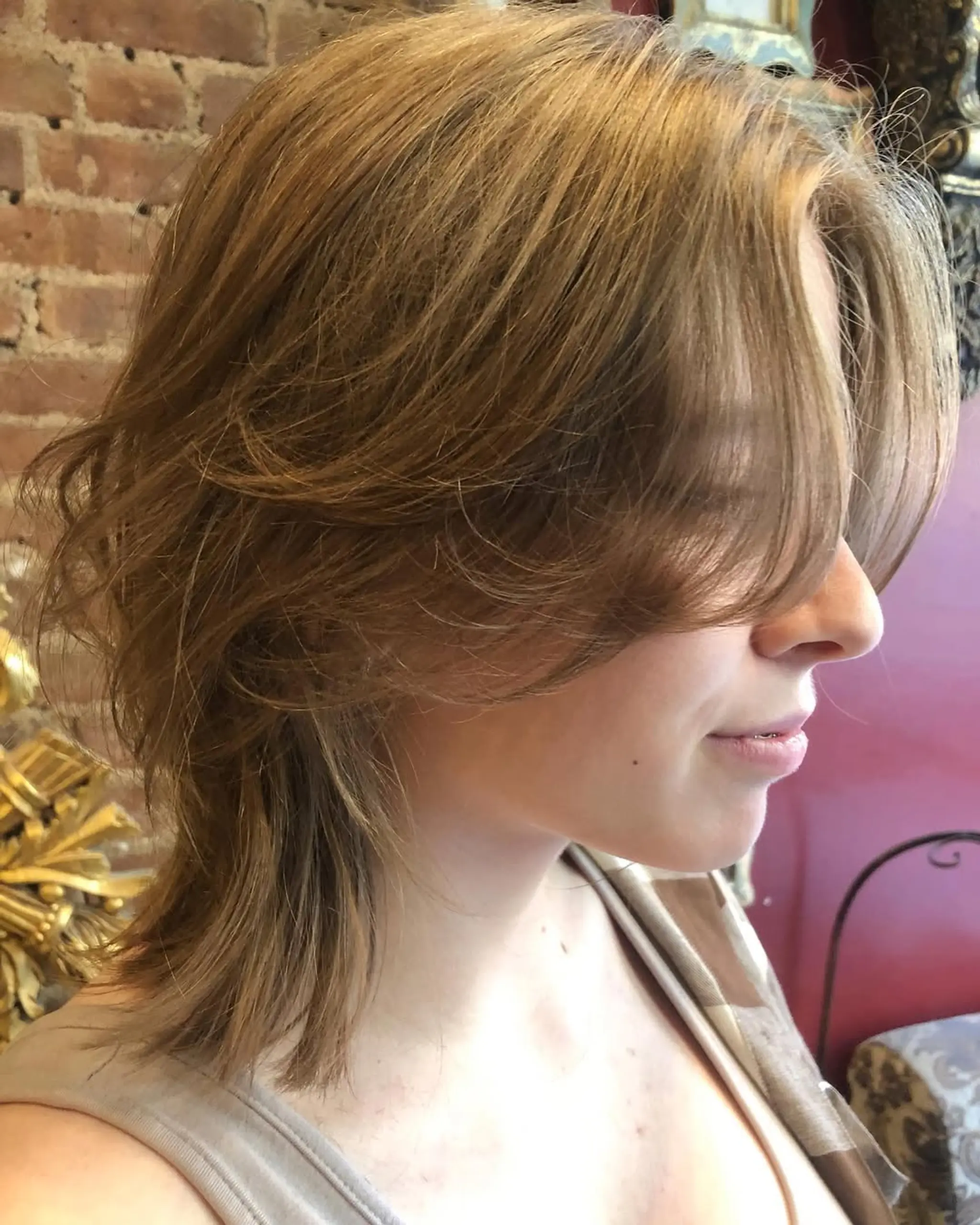 A medium-length, light brown style with wavy layers and side-swept bangs, featuring textured ends for added volume and movement.