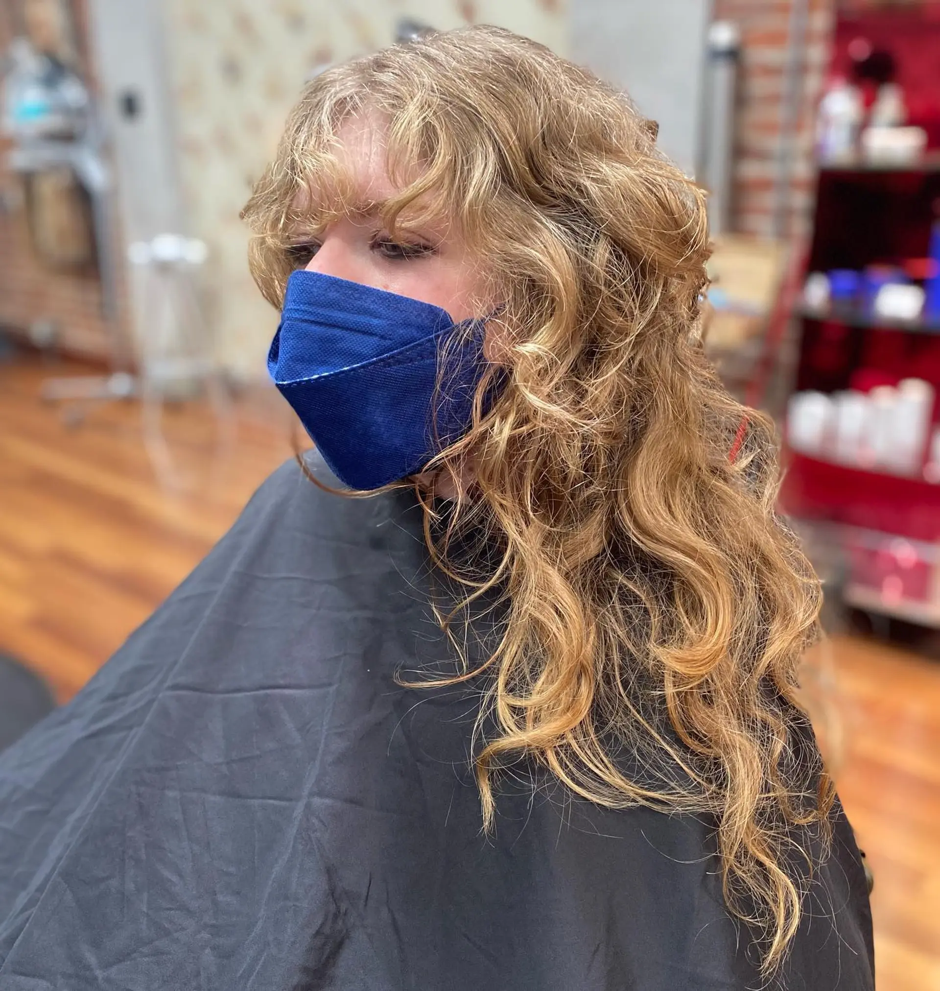 A textured, long curly shag haircut featuring full wavy bangs and heavy layering throughout for added volume and movement. 1