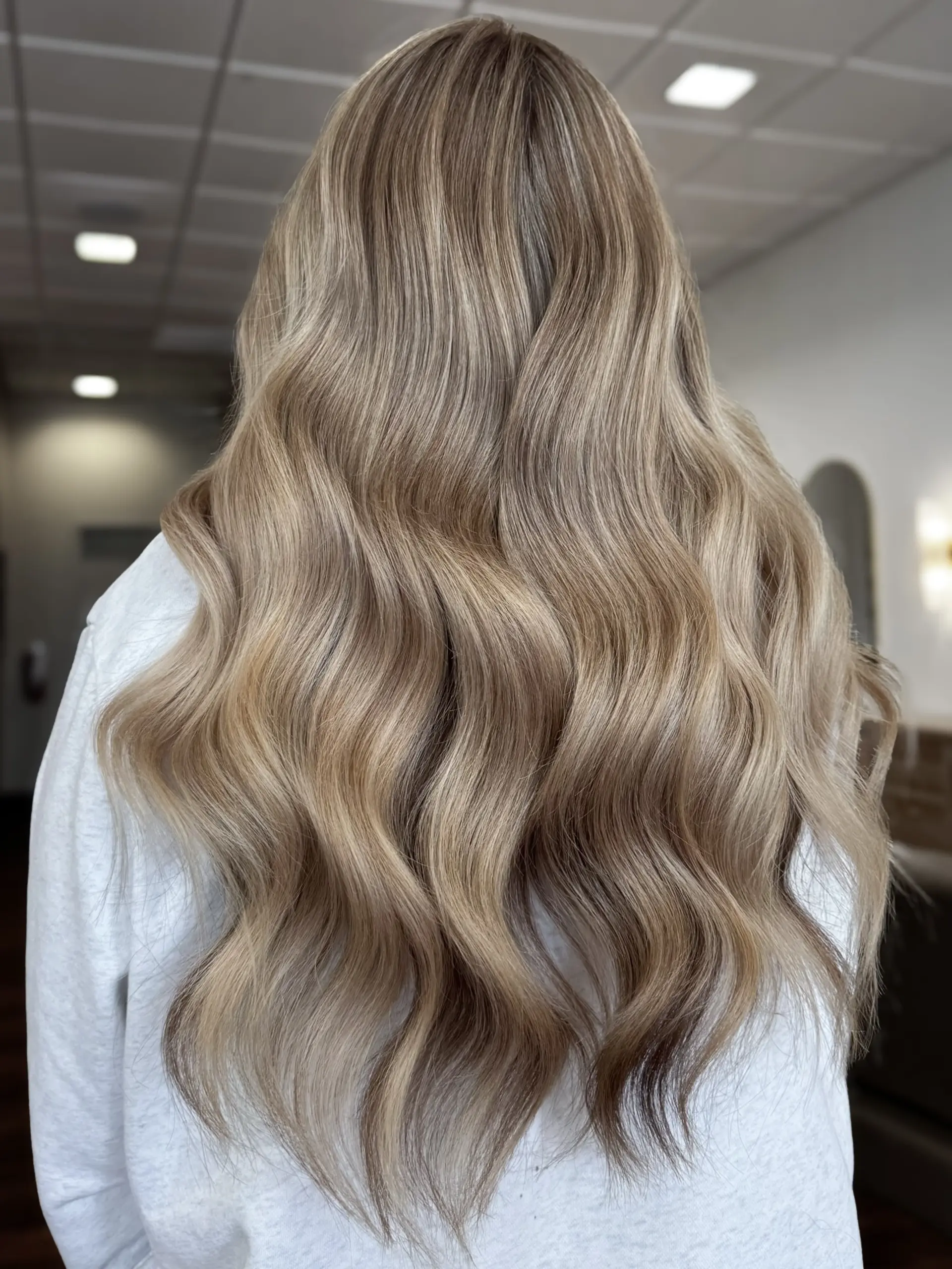 Long, flowing dimensional blonde hair styled into soft, elegant waves. 1