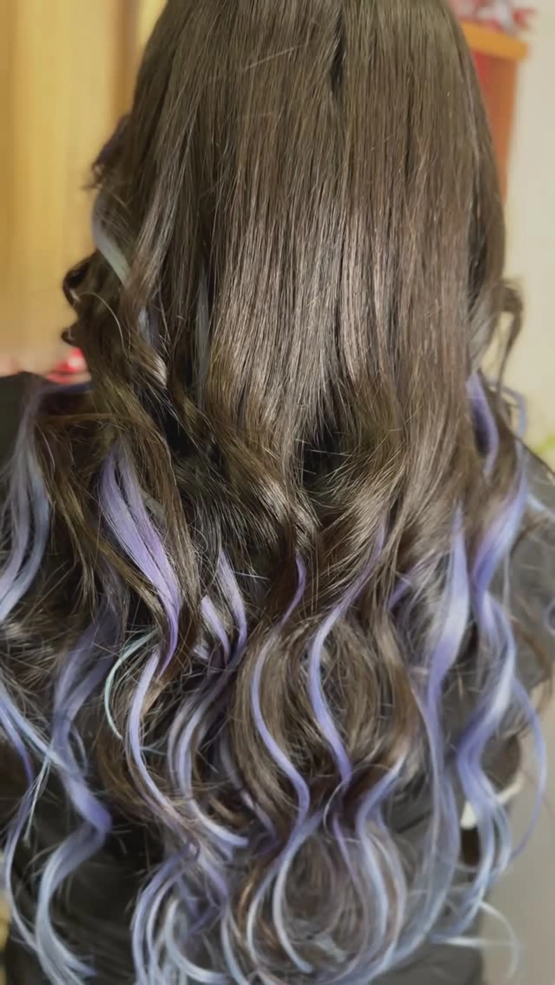 Long dark brown hair styled with defined waves featuring pastel lavender and periwinkle peekaboo highlights. 1