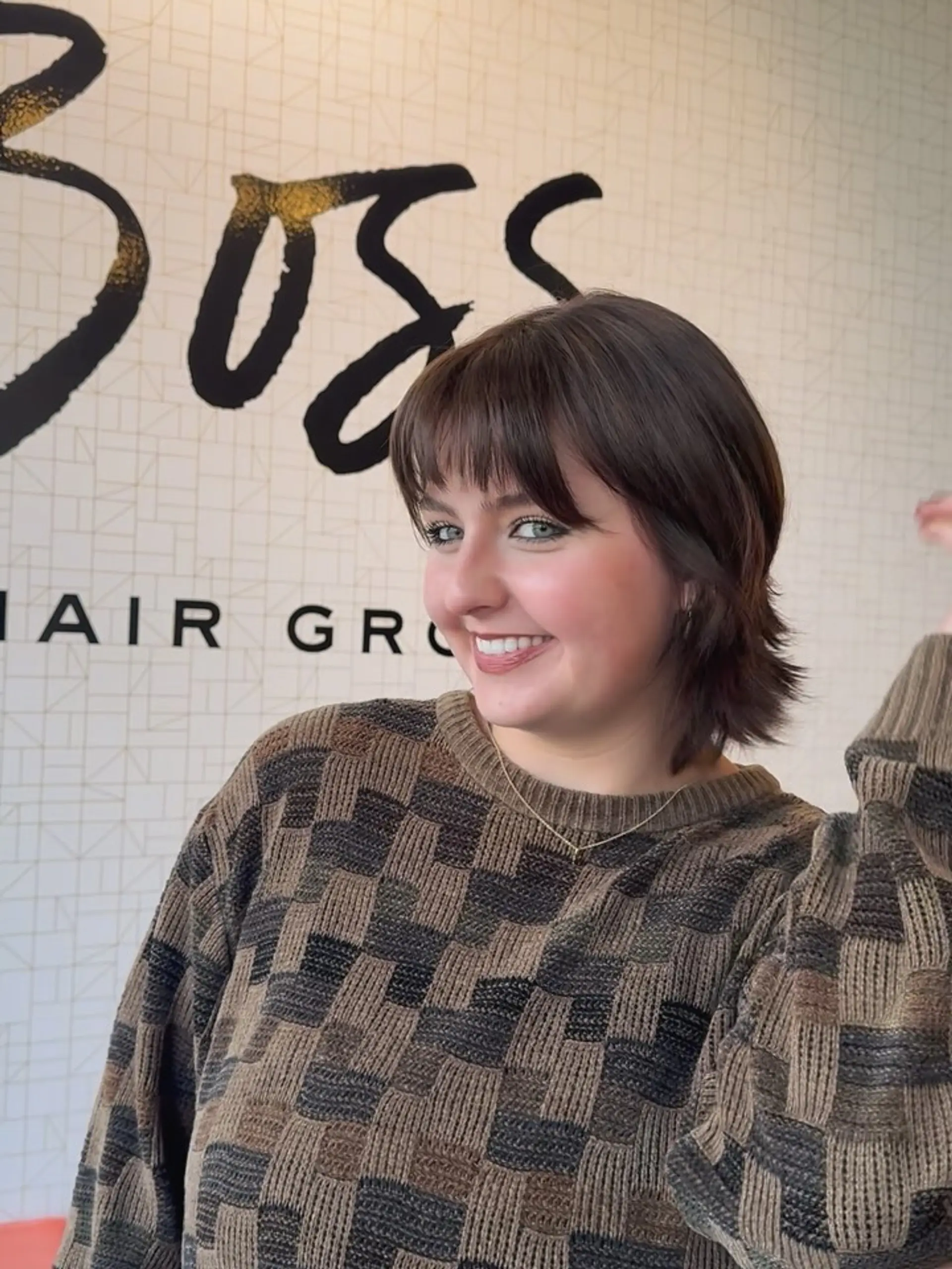 A short, textured shag haircut featuring brow-skimming full bangs and flipped, wispy layers, finished in a rich chocolate brown tone. 1