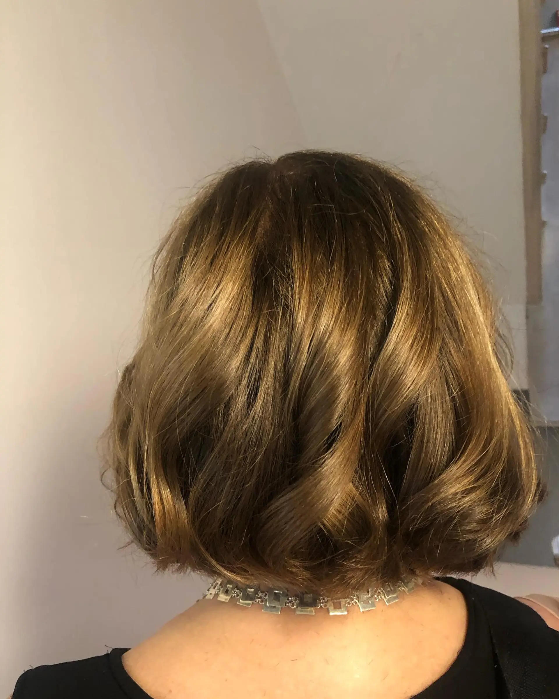 A short, neck-length bob styled with soft waves and curls in a lustrous golden brown tone. 1