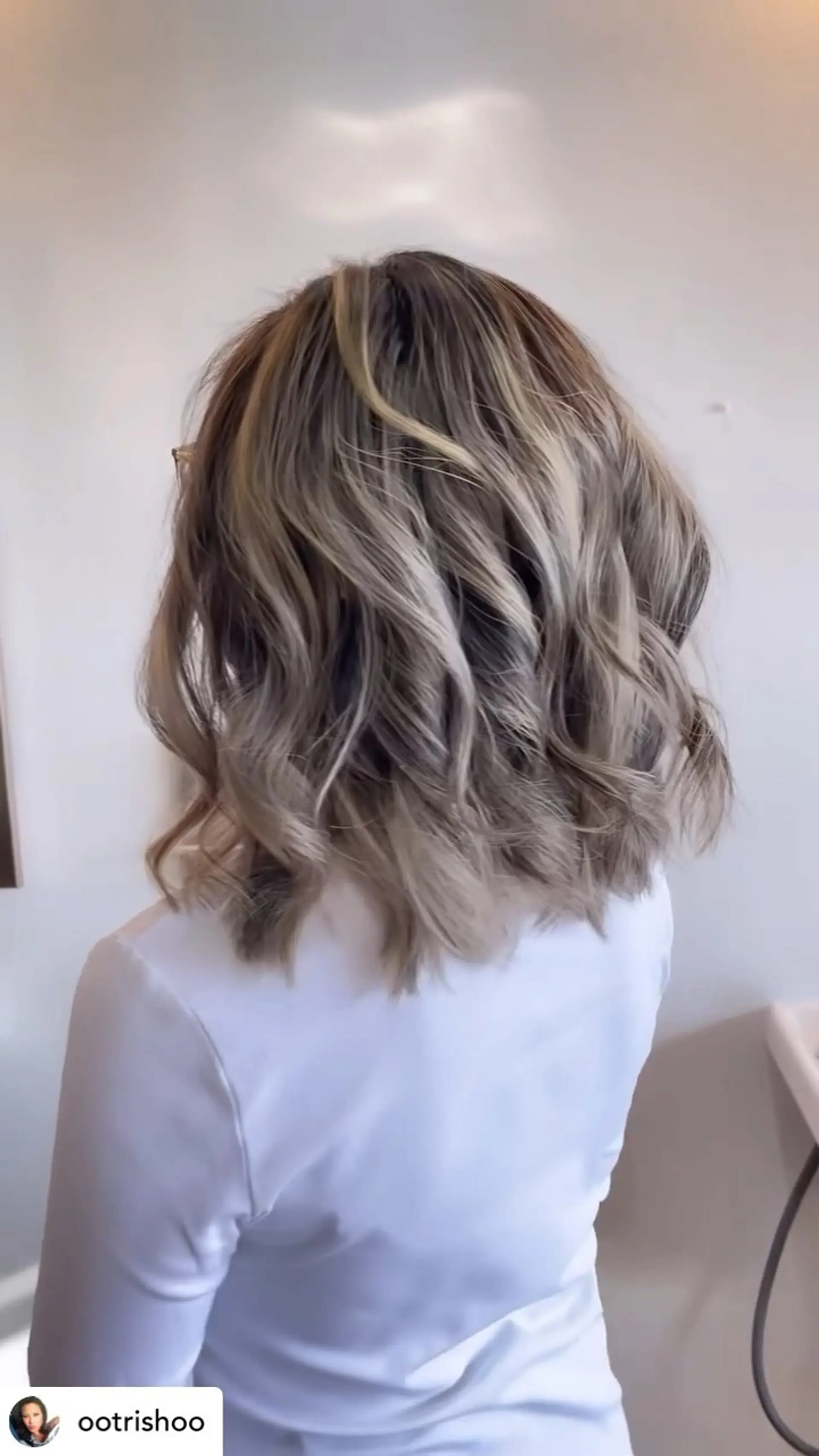 Shoulder-length textured lob with cool ash blonde highlights, styled in soft, loose waves. 1