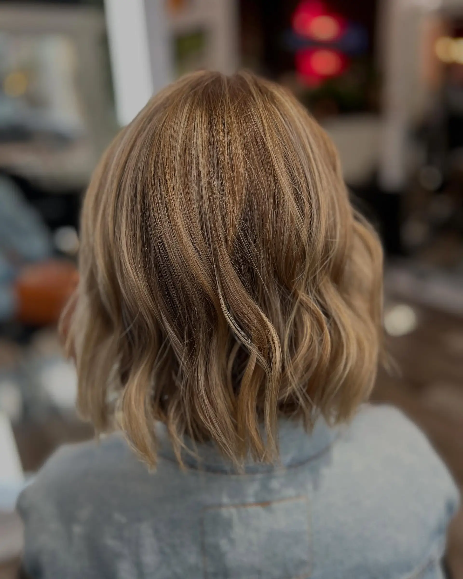A textured, neck-length bob cut styled in relaxed, lived-in waves featuring soft dimensional warm blonde highlights over a neutral base. 1