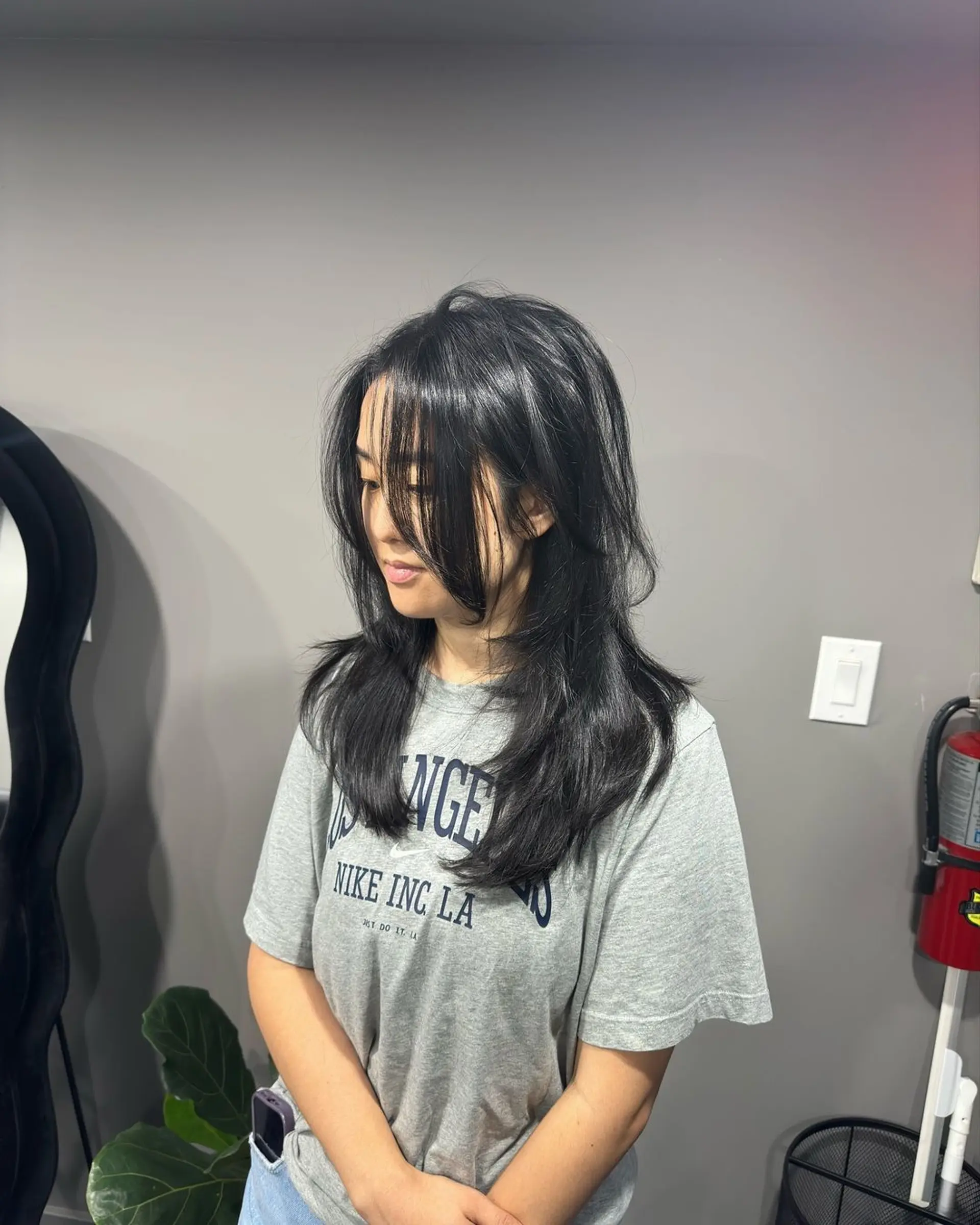 Medium-length black hair with voluminous layers and side-swept bangs that give a tousled and casual look. 2