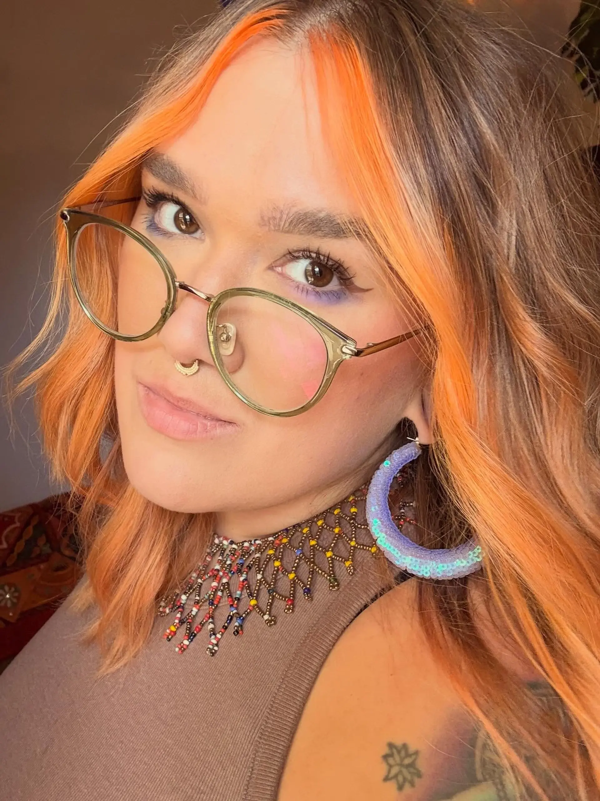 Medium-length wavy hair featuring a vibrant neon orange money piece framing the face against warm brown tones. 1
