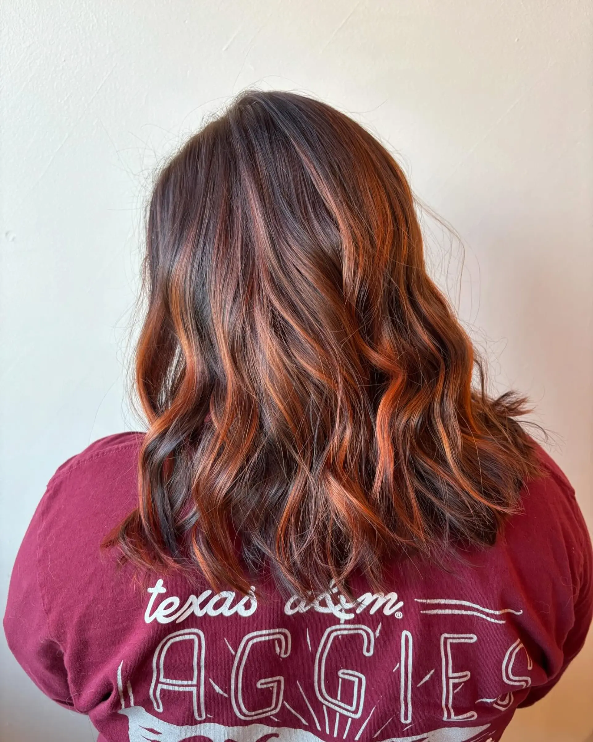 Medium-length wavy brunette hair enhanced with warm, vibrant copper hand-painted balayage ribbons. 1