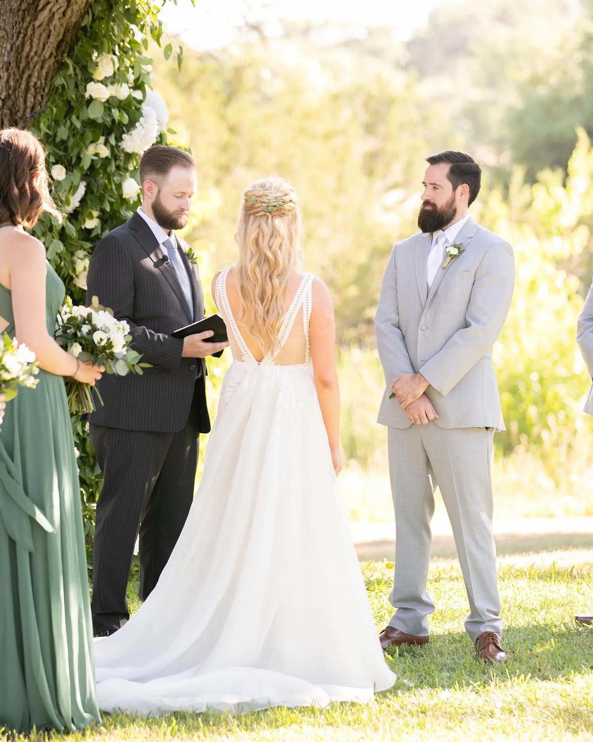 A romantic half-up bridal hairstyle featuring a crown braid accented with greenery and flowing soft waves. 1