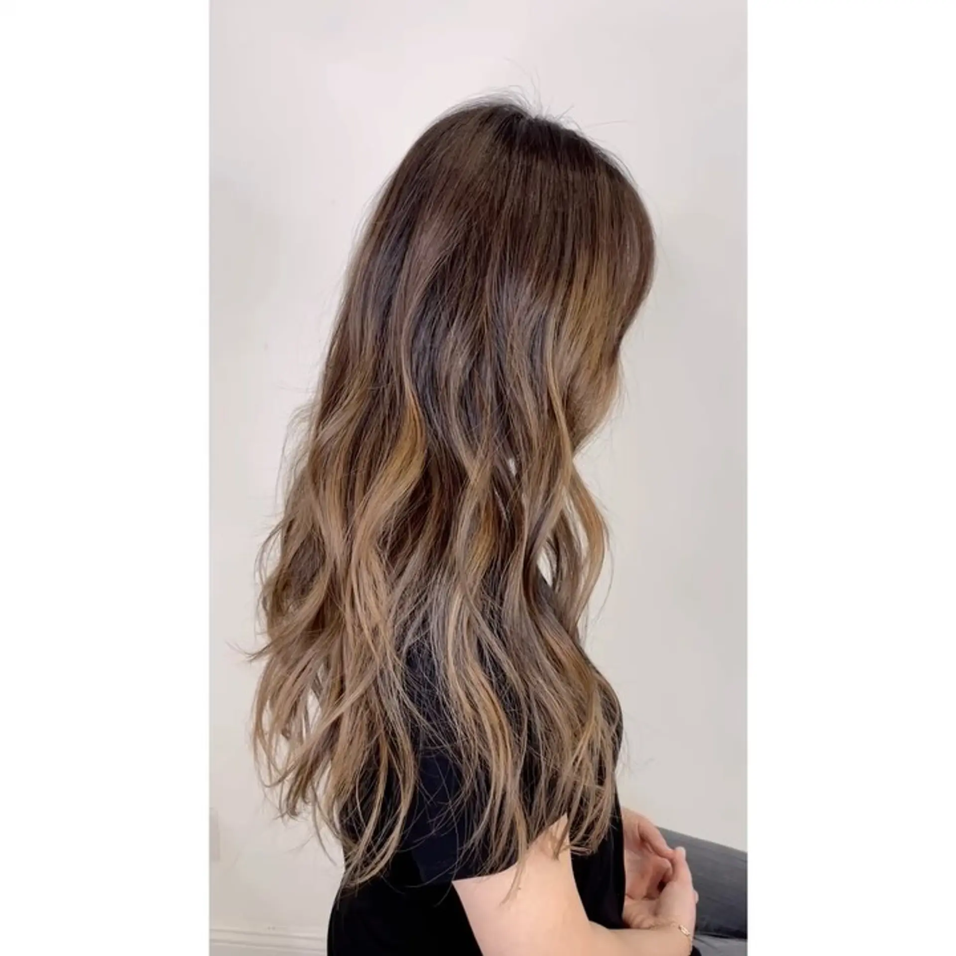 Long dimensional waves featuring a dark brunette base seamlessly blended into warm caramel and soft blonde balayage highlights. 1