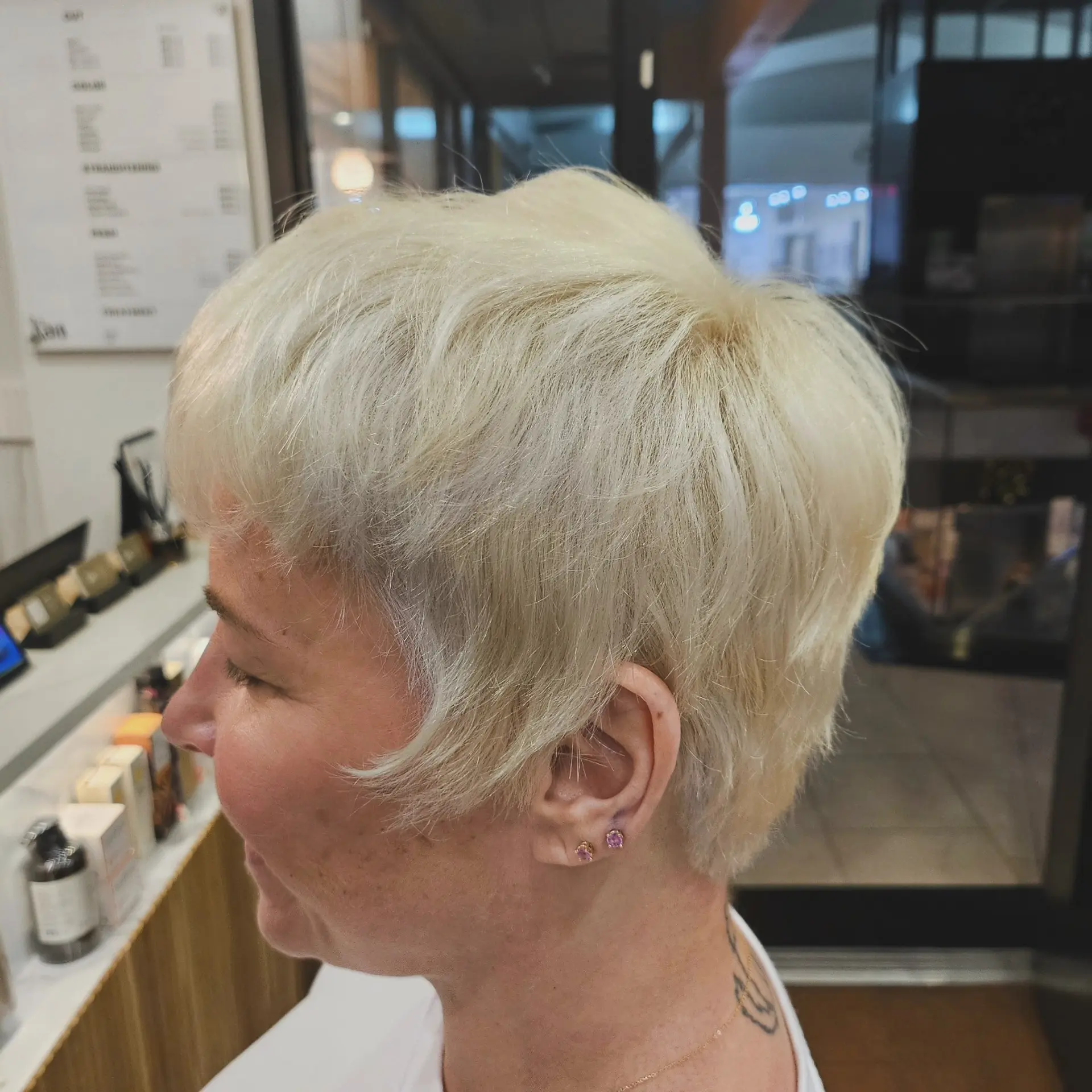 A soft, textured platinum blonde pixie haircut with feathered bangs and softly tapered sides. 1