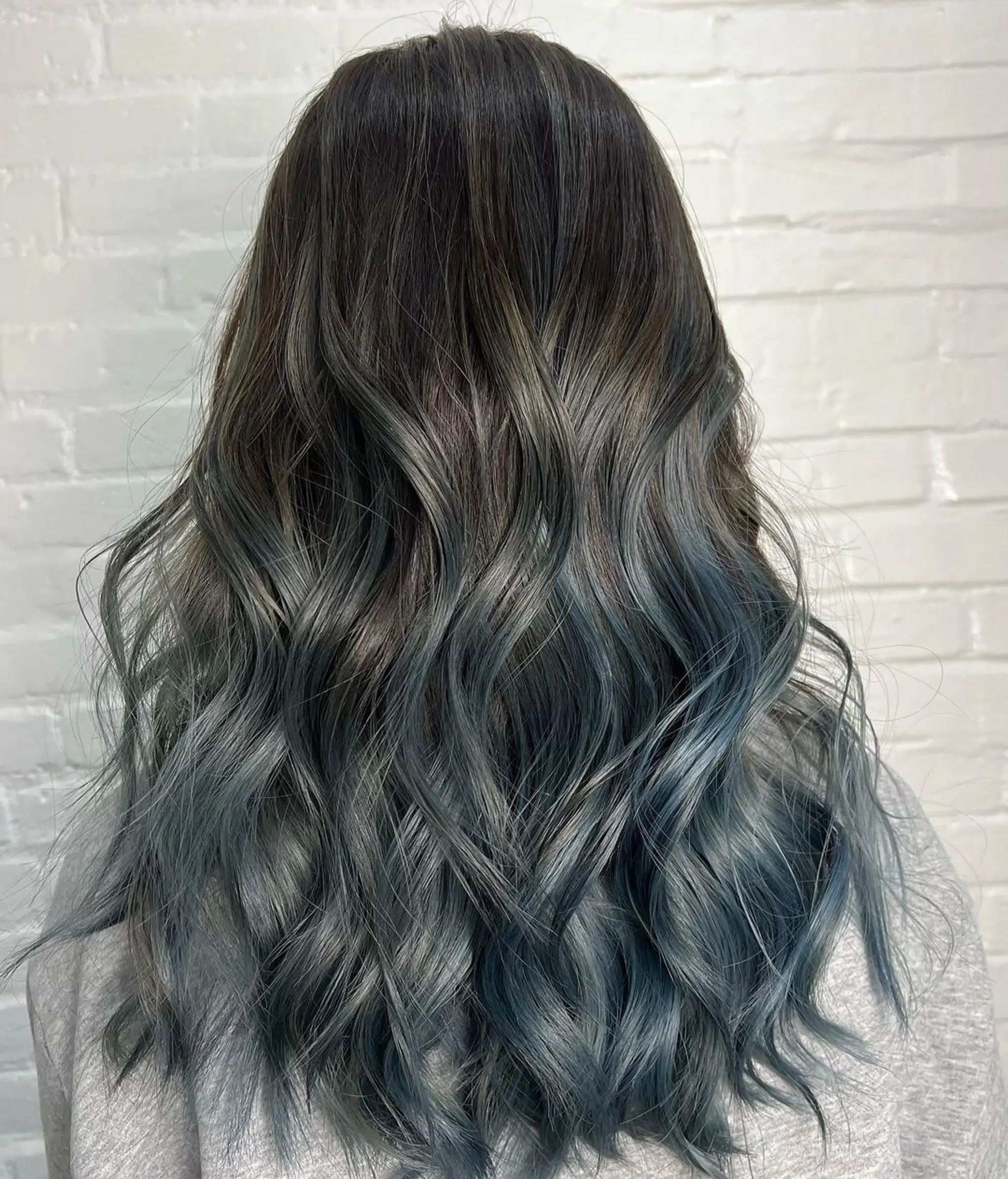 Long, wavy hair with a dark brown base transitioning into a vibrant blue gradient. Soft waves and a seamless balayage technique.
