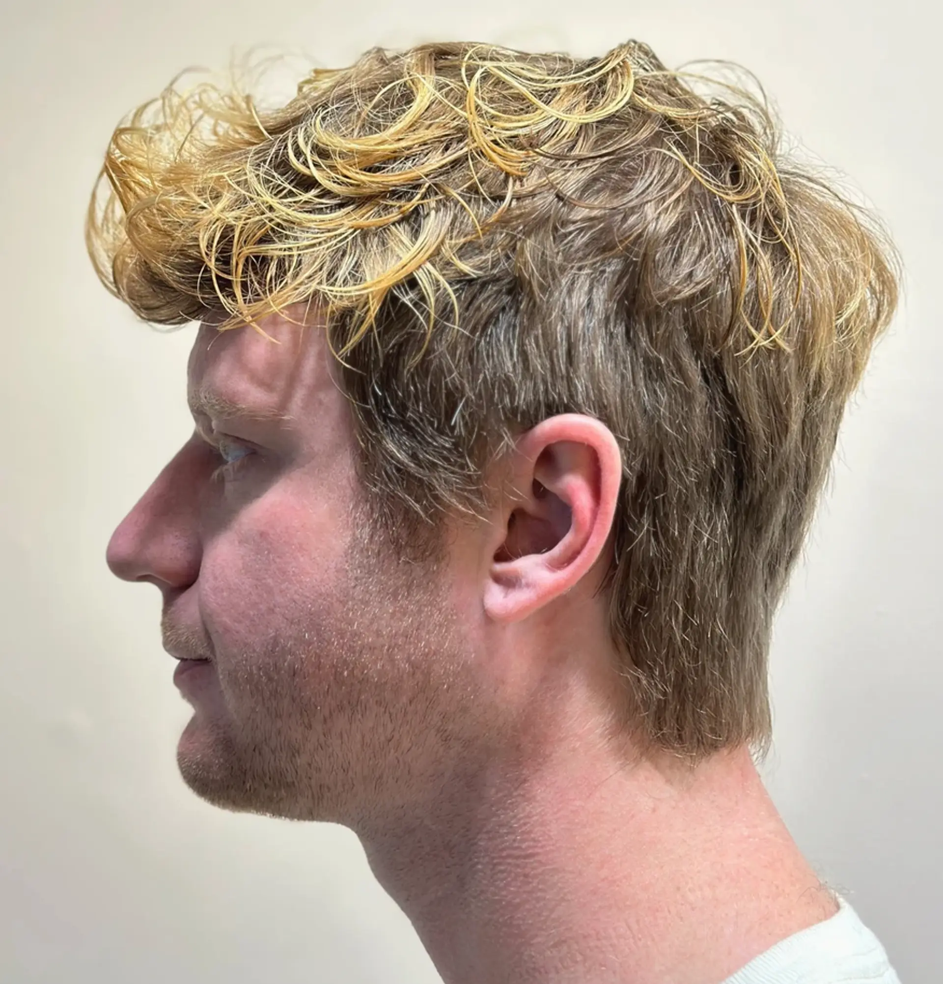 A short, wavy haircut with light brown tones and sun-kissed blonde highlights, featuring tousled waves and casual layers for a natural and relaxed appearance. 1