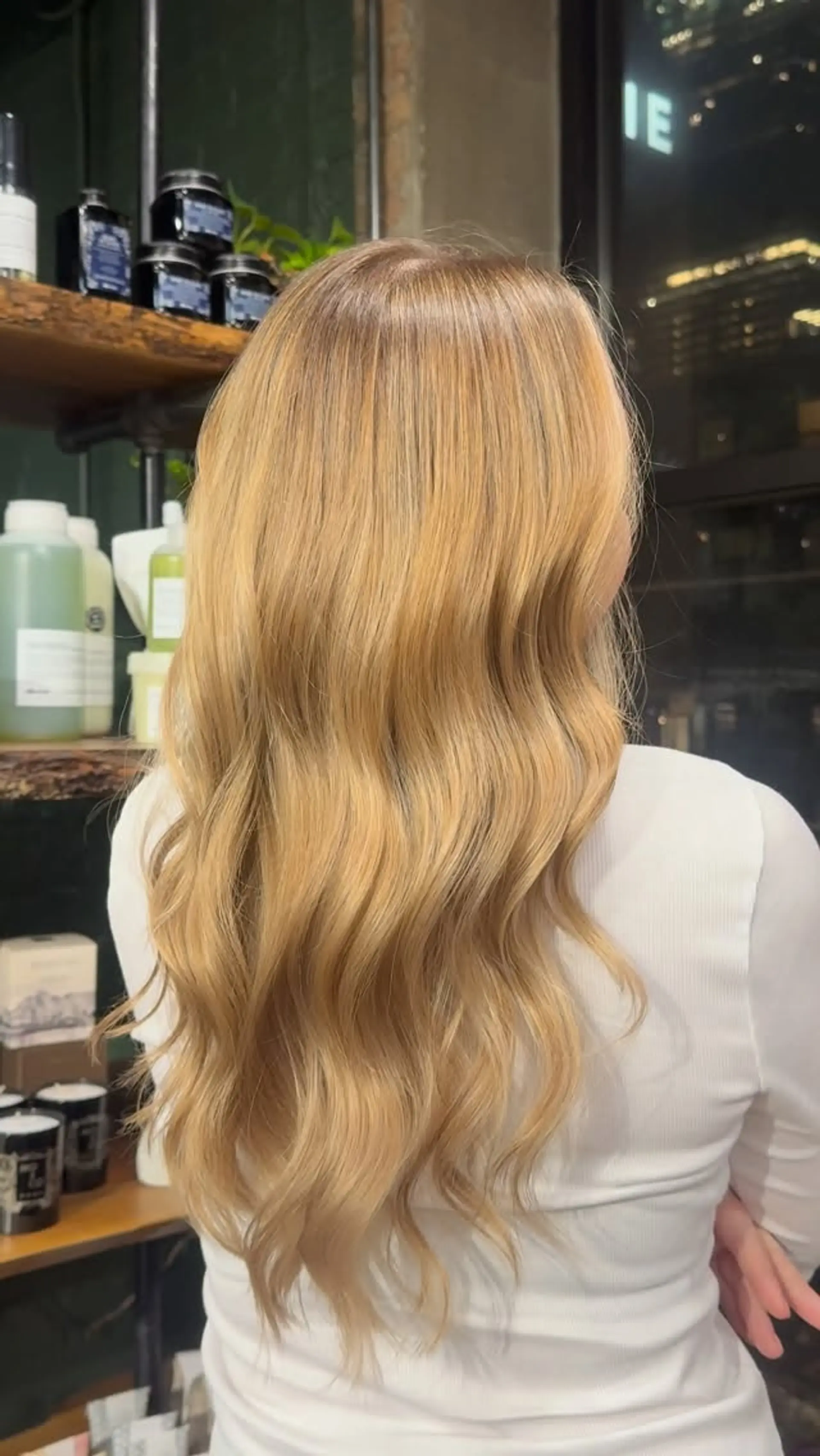 Long warm golden blonde hair styled into smooth, flowing waves cascading down the back. 1
