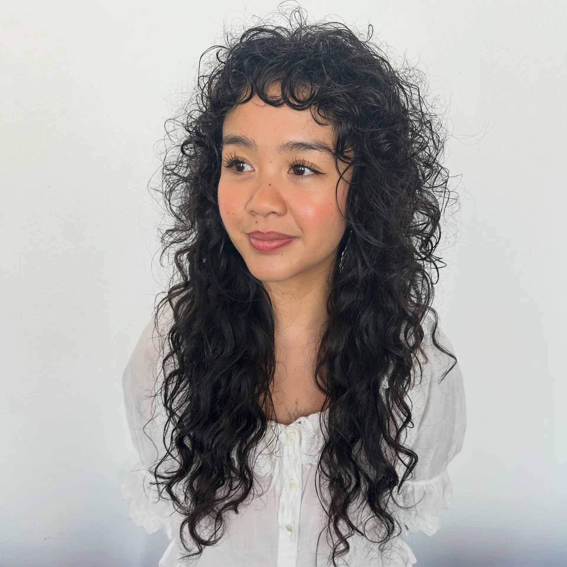 Long, naturally curly dark hair cut into a textured shag with defined ringlets and short curly bangs. 1