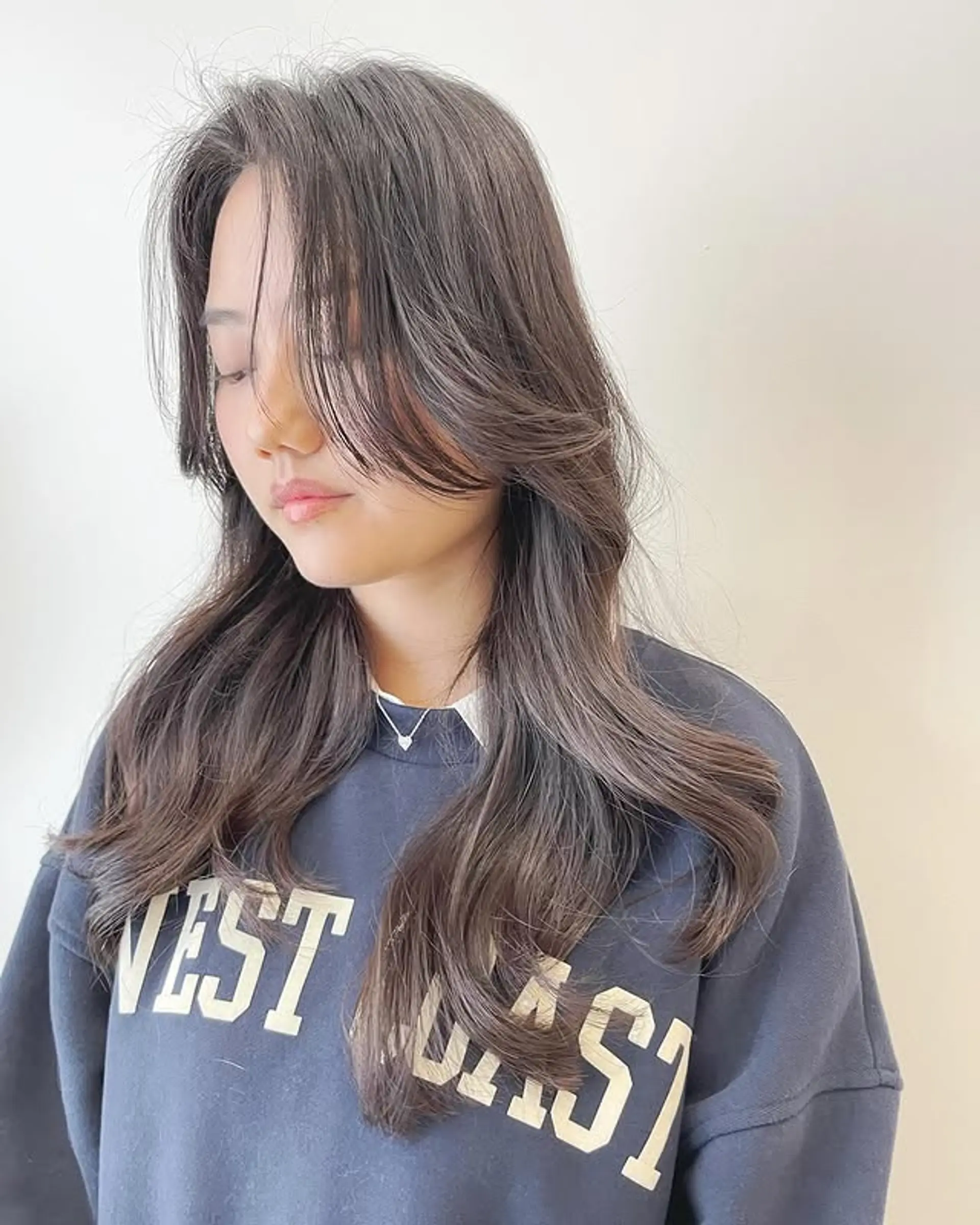 A long layered haircut with subtle waves and face-framing curtain bangs. 1