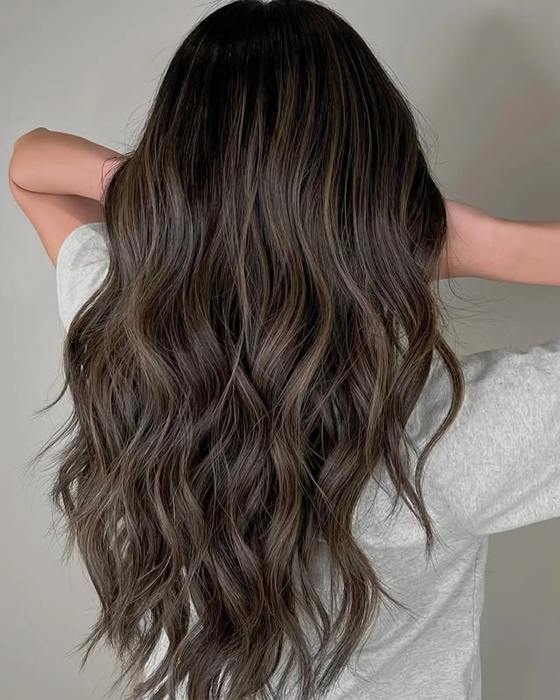 A model with long wavy hair showcasing the Expensive Brunette Balayage trend with dimensional, subtle highlights. - Preview 2