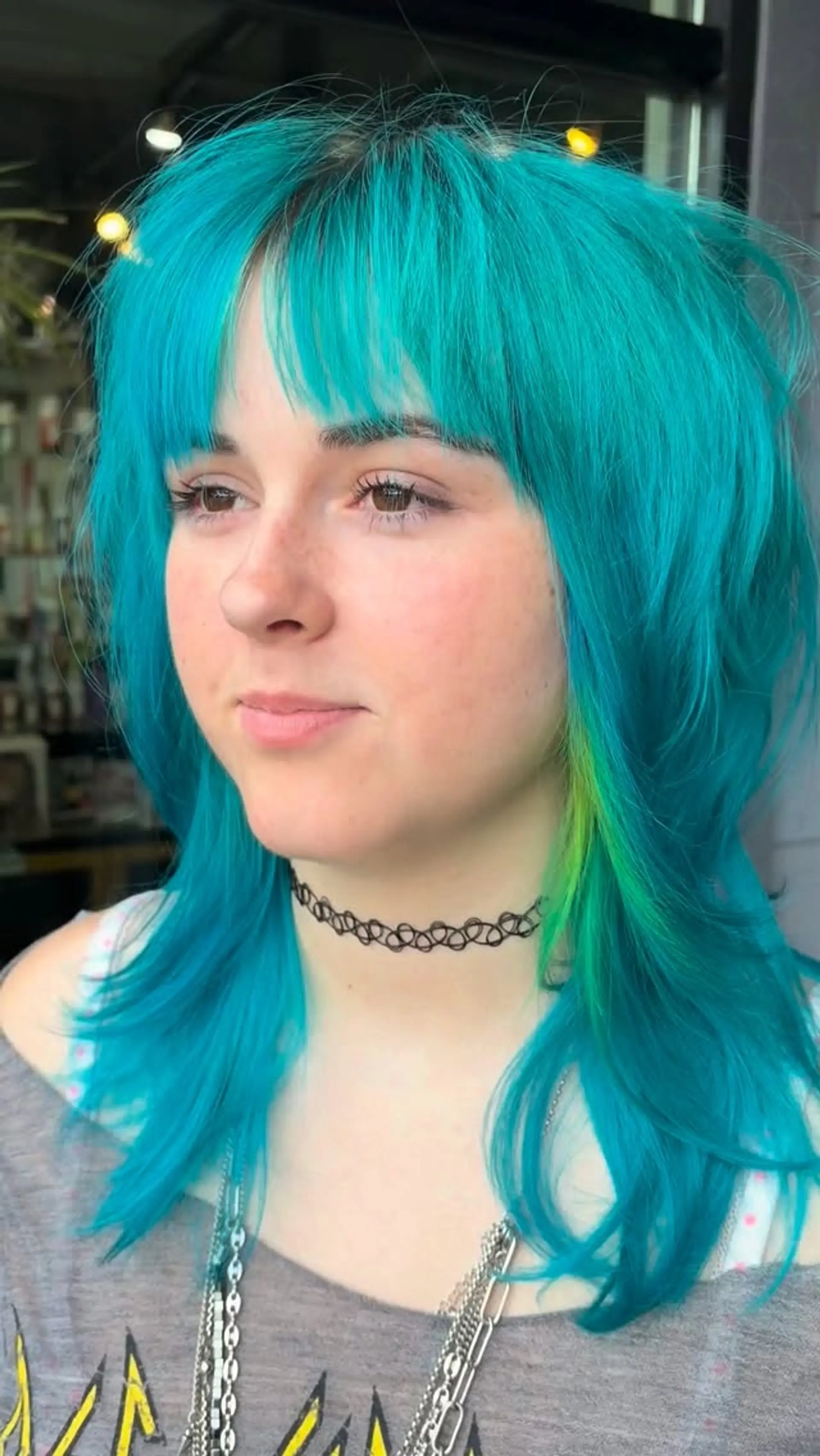 A heavily layered medium-length shag haircut with textured bangs and bright cyan-blue coloring featuring a lime green accent strand. 1