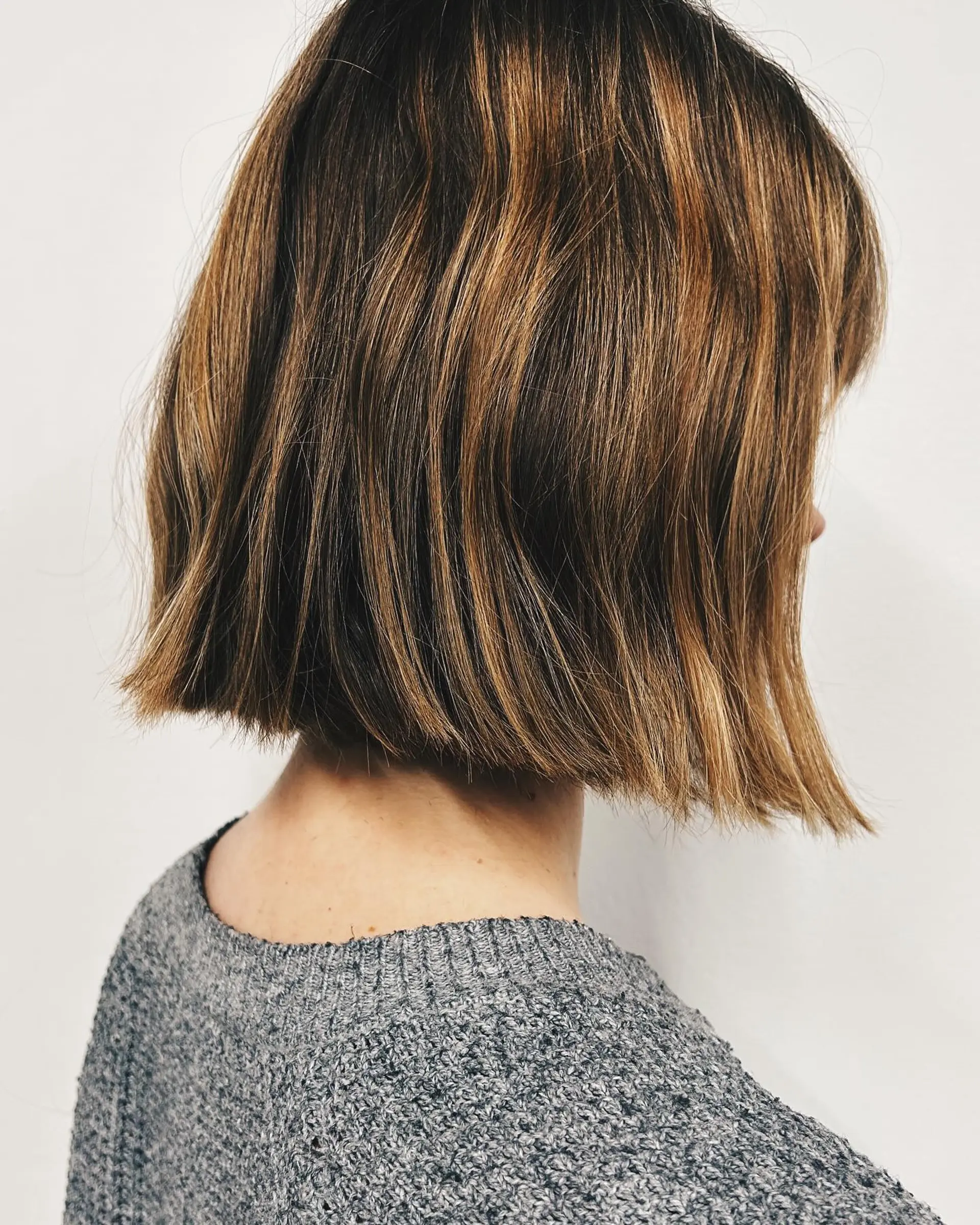 A blunt bob cut ending above the collar with subtle textured ends and natural warm highlights. 1