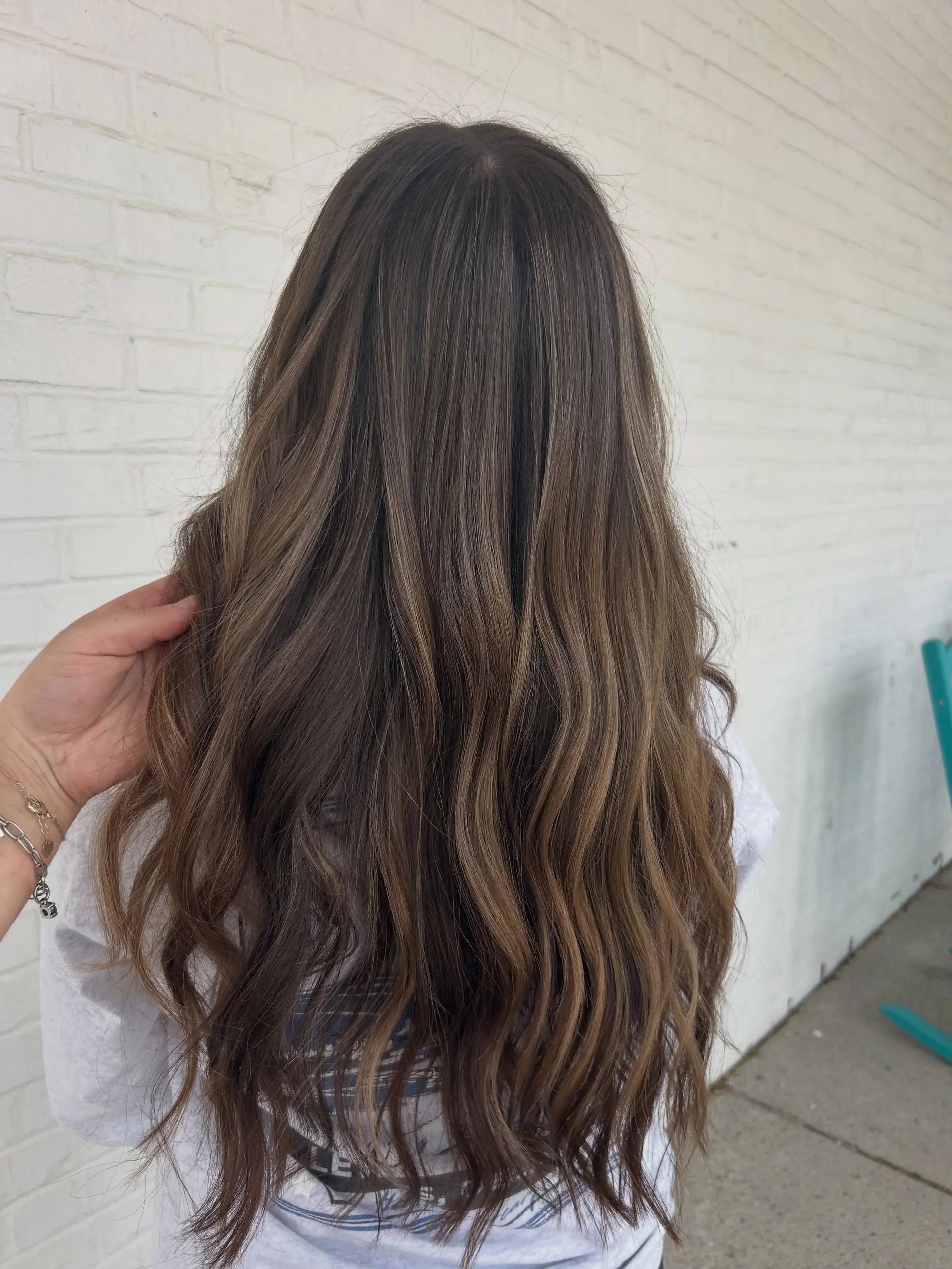 Long dimensional brunette hair styled with lived-in balayage highlights and loose waves. 1