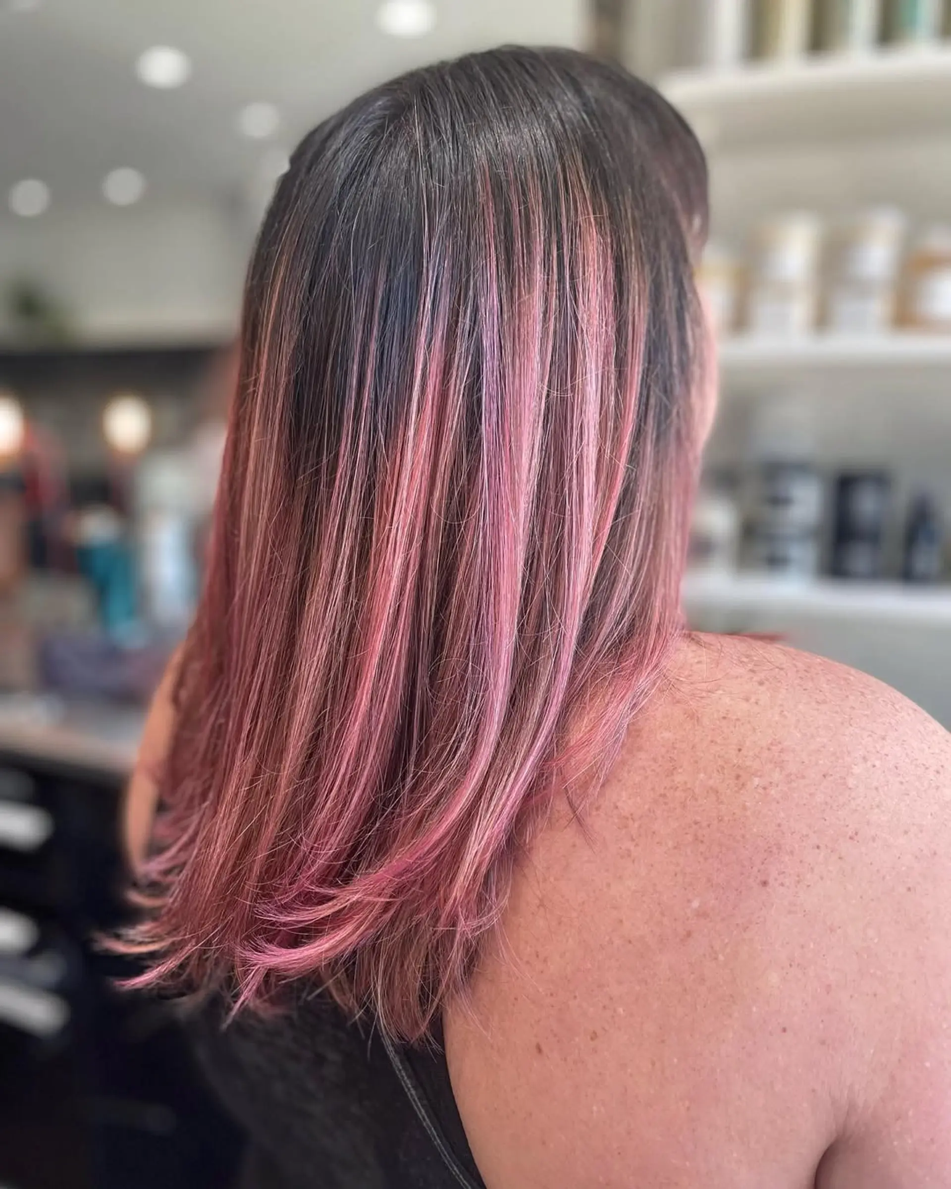 A sleek, medium-length straight hairstyle enhanced with a vibrant pink balayage that blends beautifully from dark roots, providing a dynamic and trendy dimensional color. 1