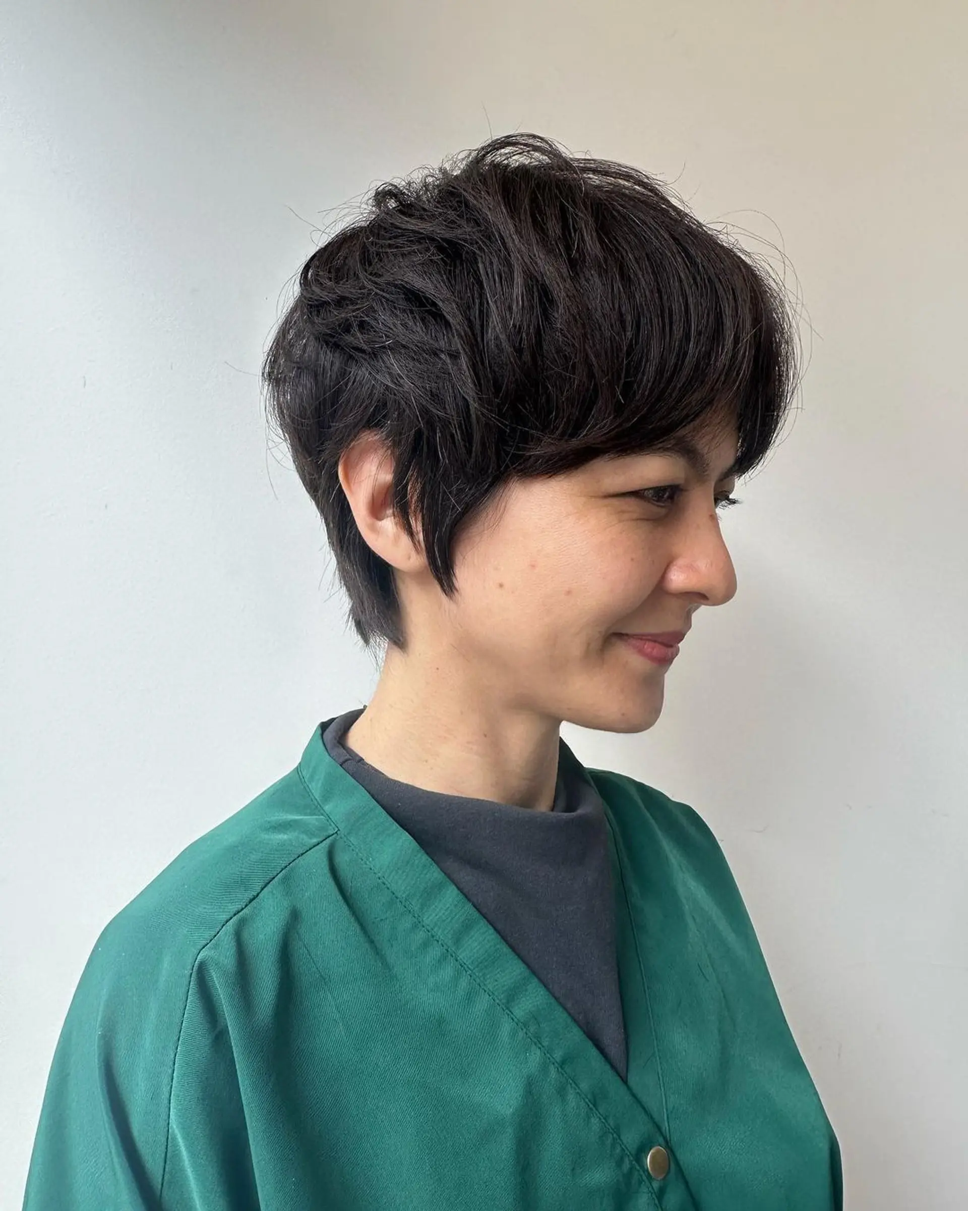 A short pixie cut with textured layers, a tapered nape, and a side-swept fringe, presenting an effortless chic style in black. 2