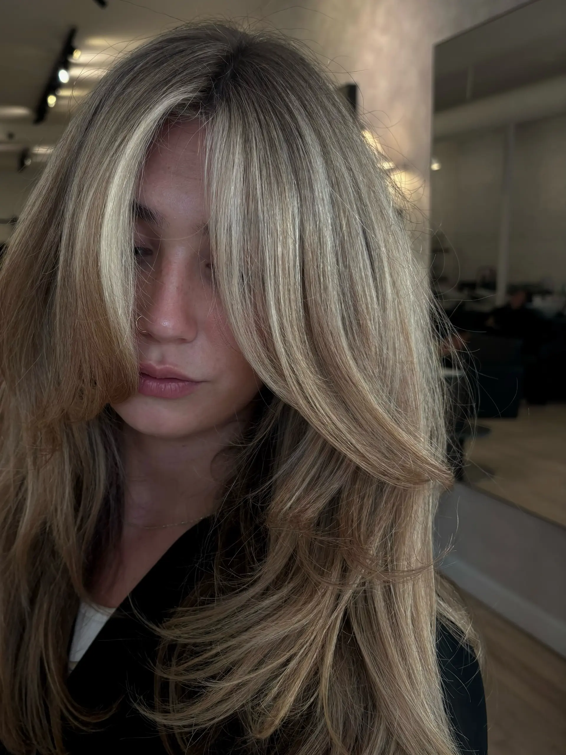 Voluminous long layered haircut featuring bright blonde dimensional highlights and curtain bangs with a soft blowout finish. 1