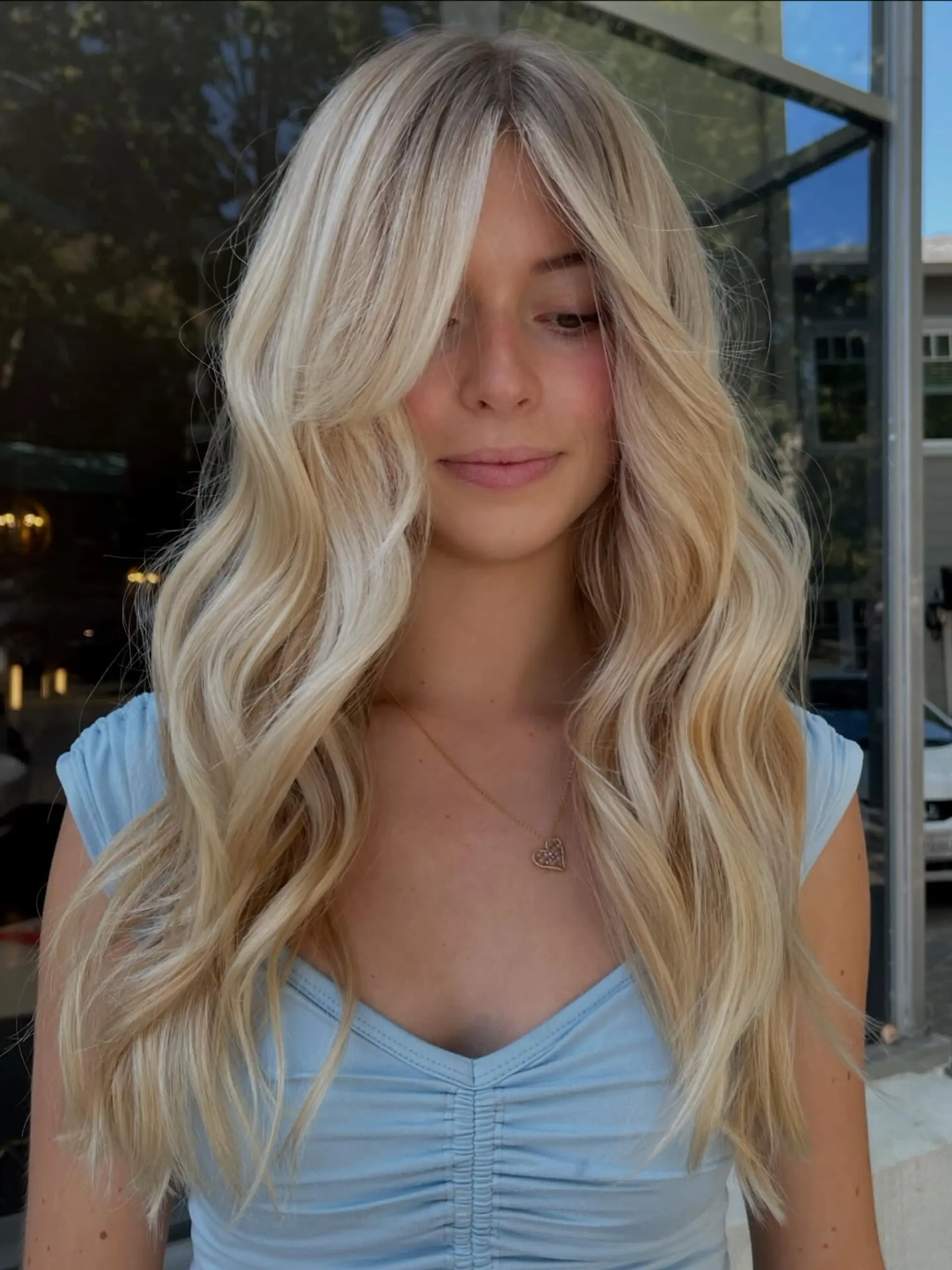 Bright lived-in blonde hair styled in soft, flowing waves with long curtain bangs framing the face. 1