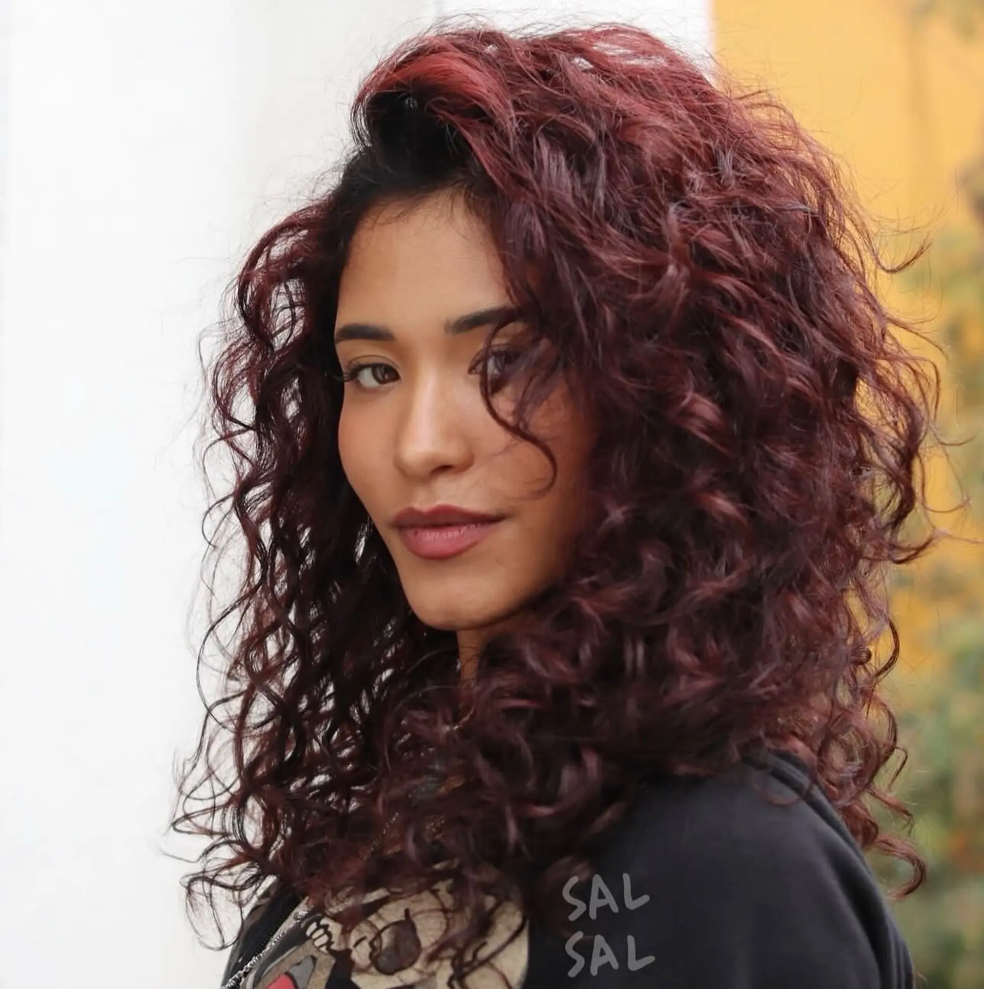 Medium-length layered curly hairstyle featuring rich burgundy-red tones and maximum natural volume. 1