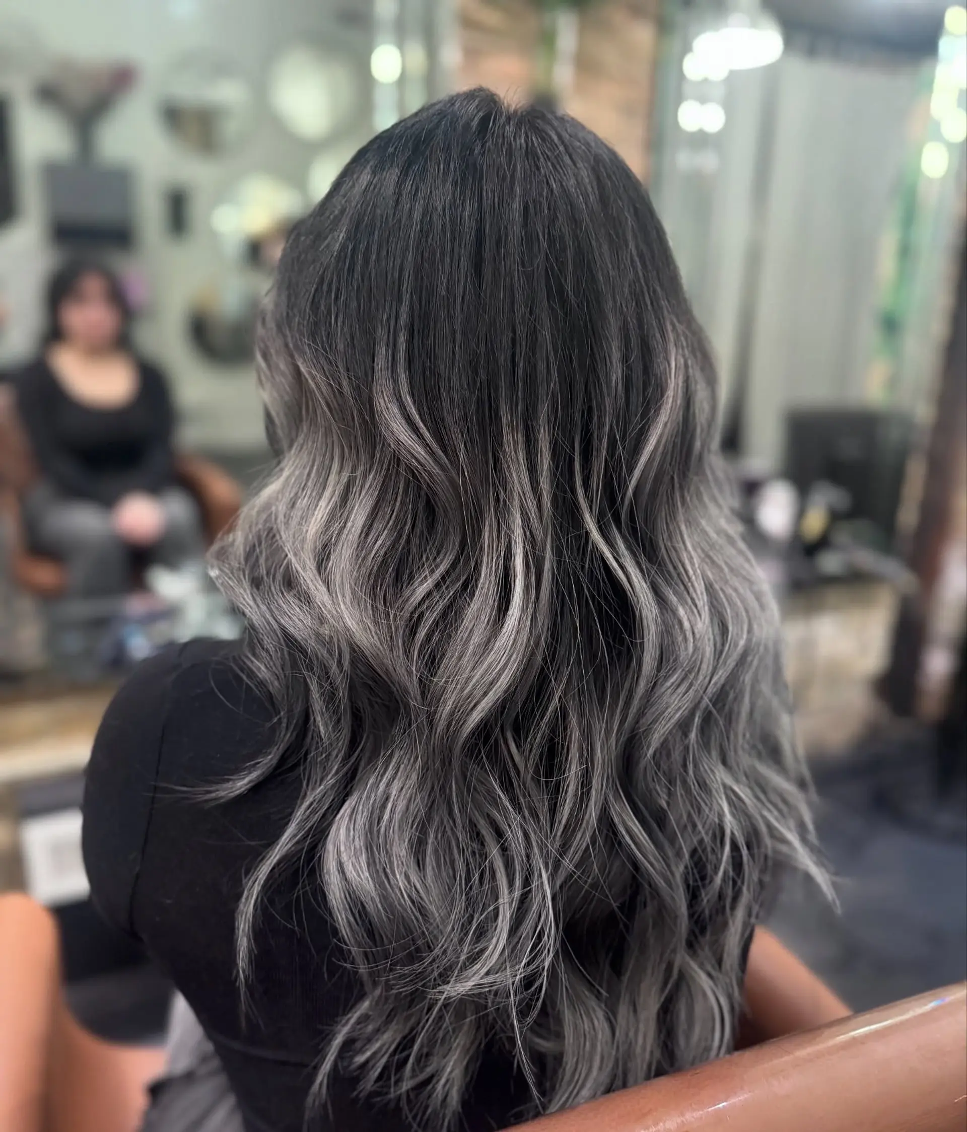 Long dark hair seamlessly blended with cool-toned ash gray and silver balayage highlights styled in loose waves. 1