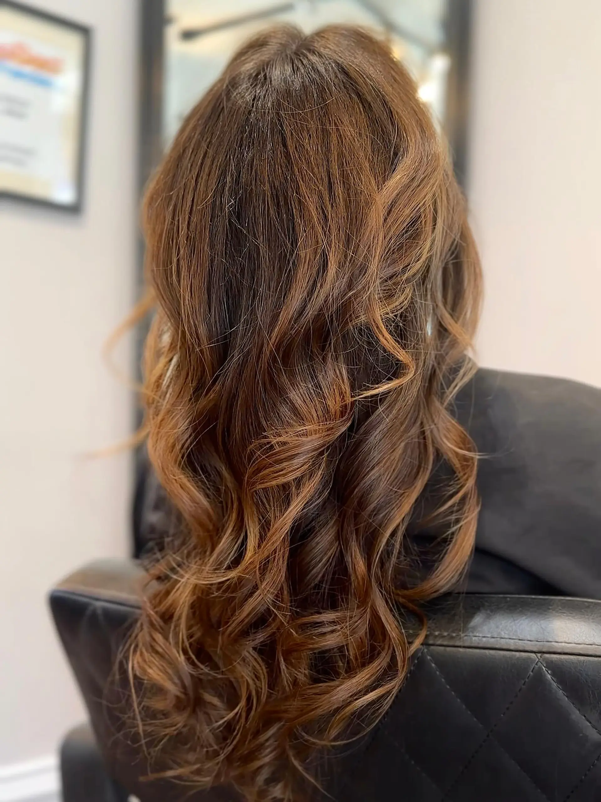 Long warm brown hair cut in soft layers and styled with loose, polished waves that add dimension and movement. 1