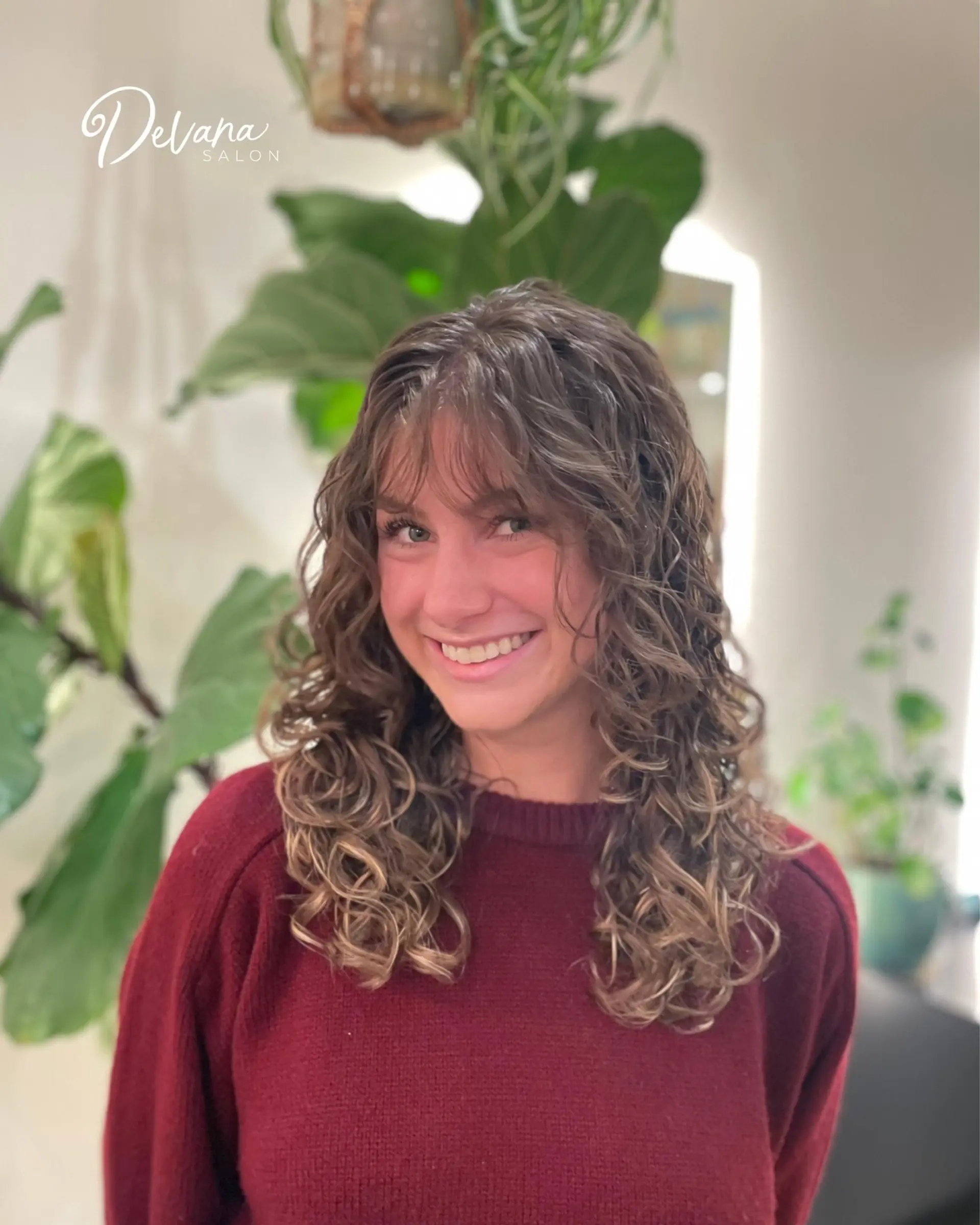 Medium-length layered curly hairstyle featuring defined curls and soft, wispy bangs framing the face. 1