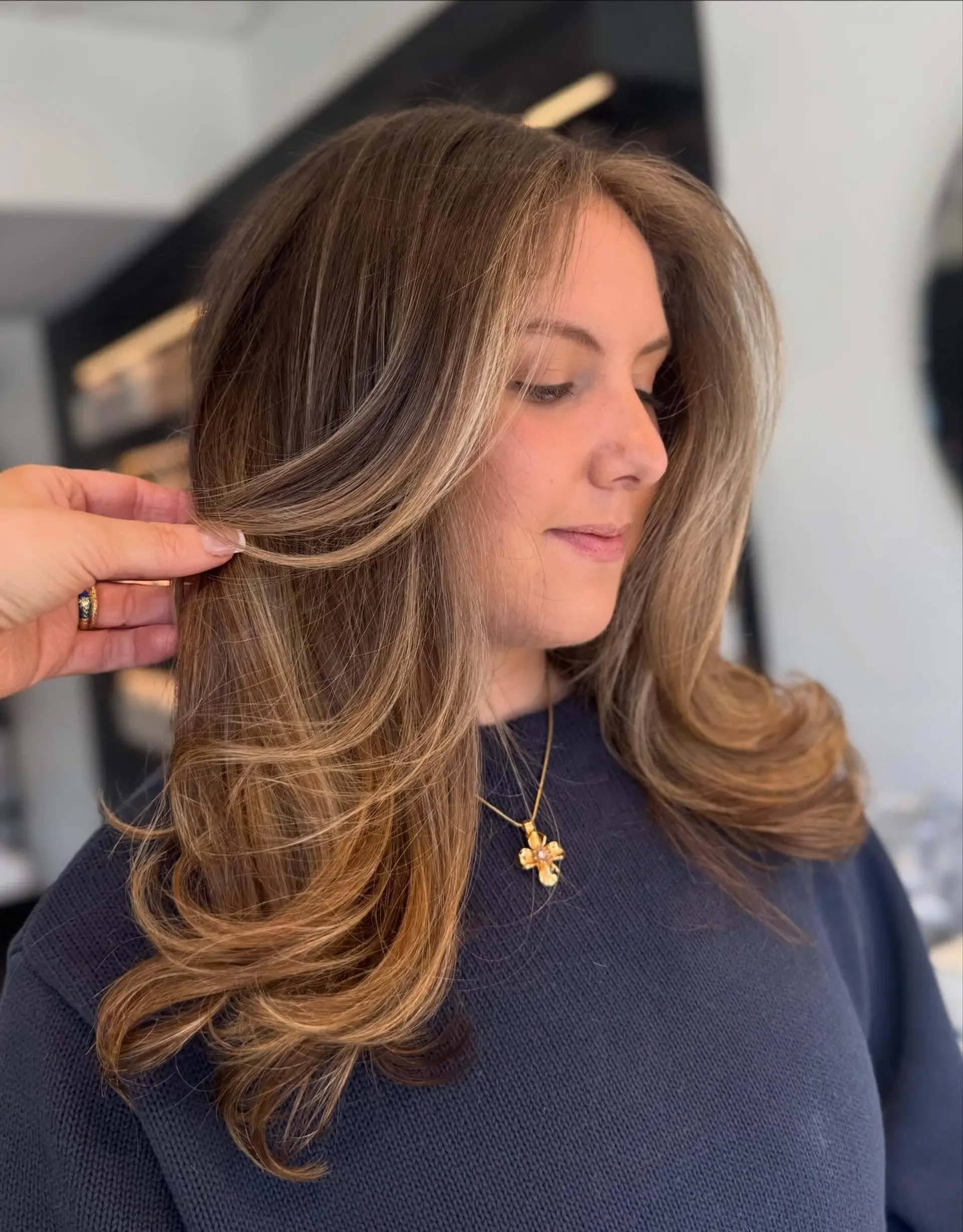 Medium-to-long layered brunette hair highlighted with warm honey and caramel balayage tones, styled into a voluminous, bouncy blowout with flipped ends. 1