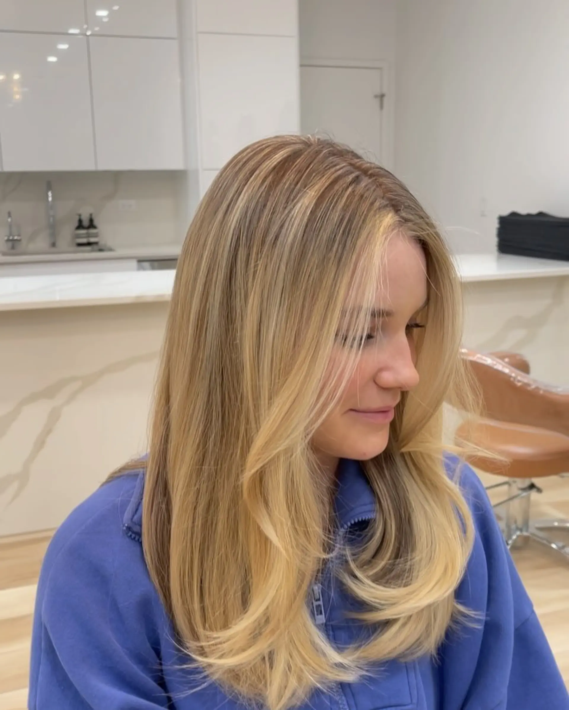 Long dimensional blonde hair featuring soft, face-framing layers styled into a smooth blowout with curled ends. 1