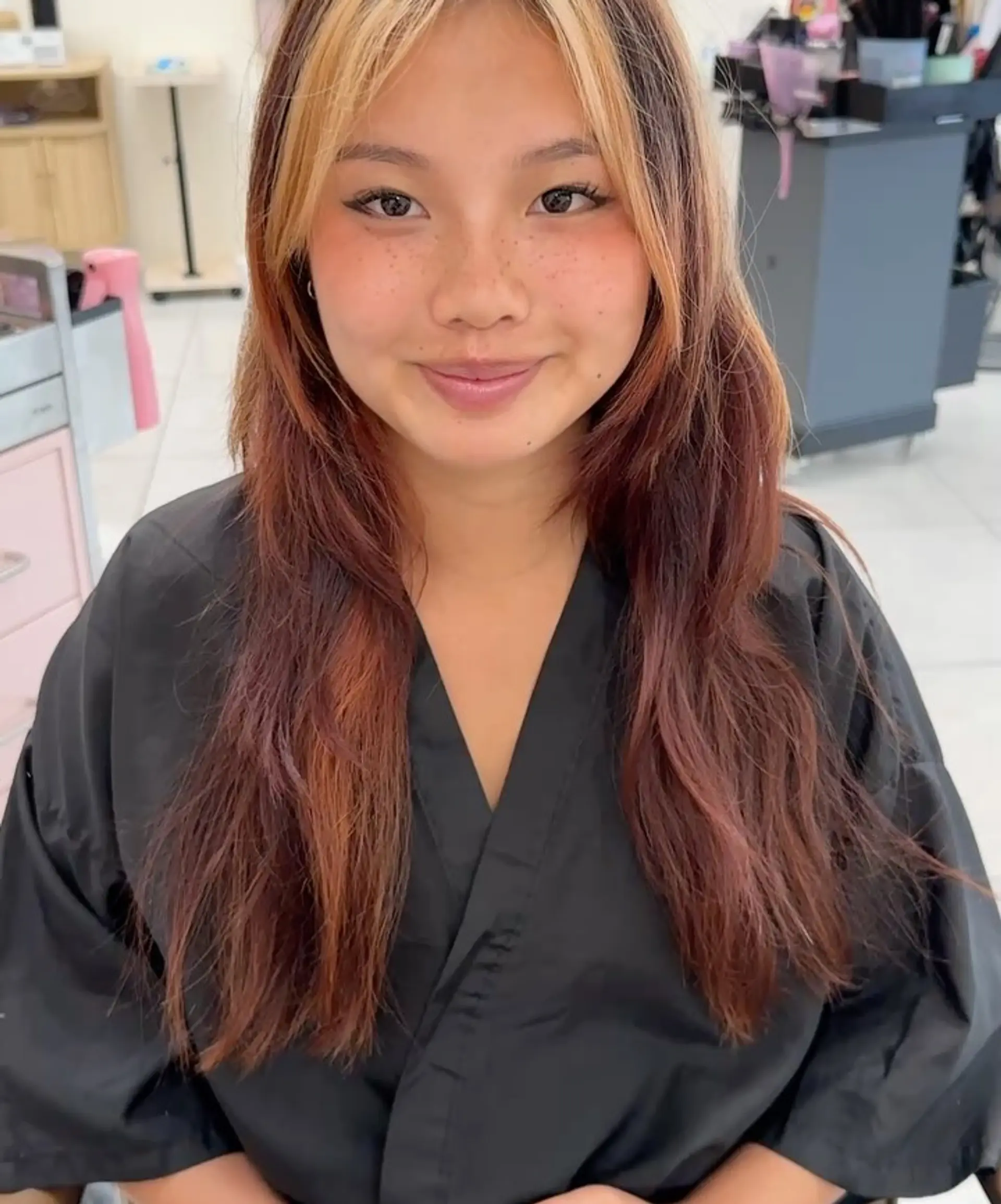 Long layered reddish-brown hair featuring a bold blonde face-framing money piece and textured curtain bangs. 1