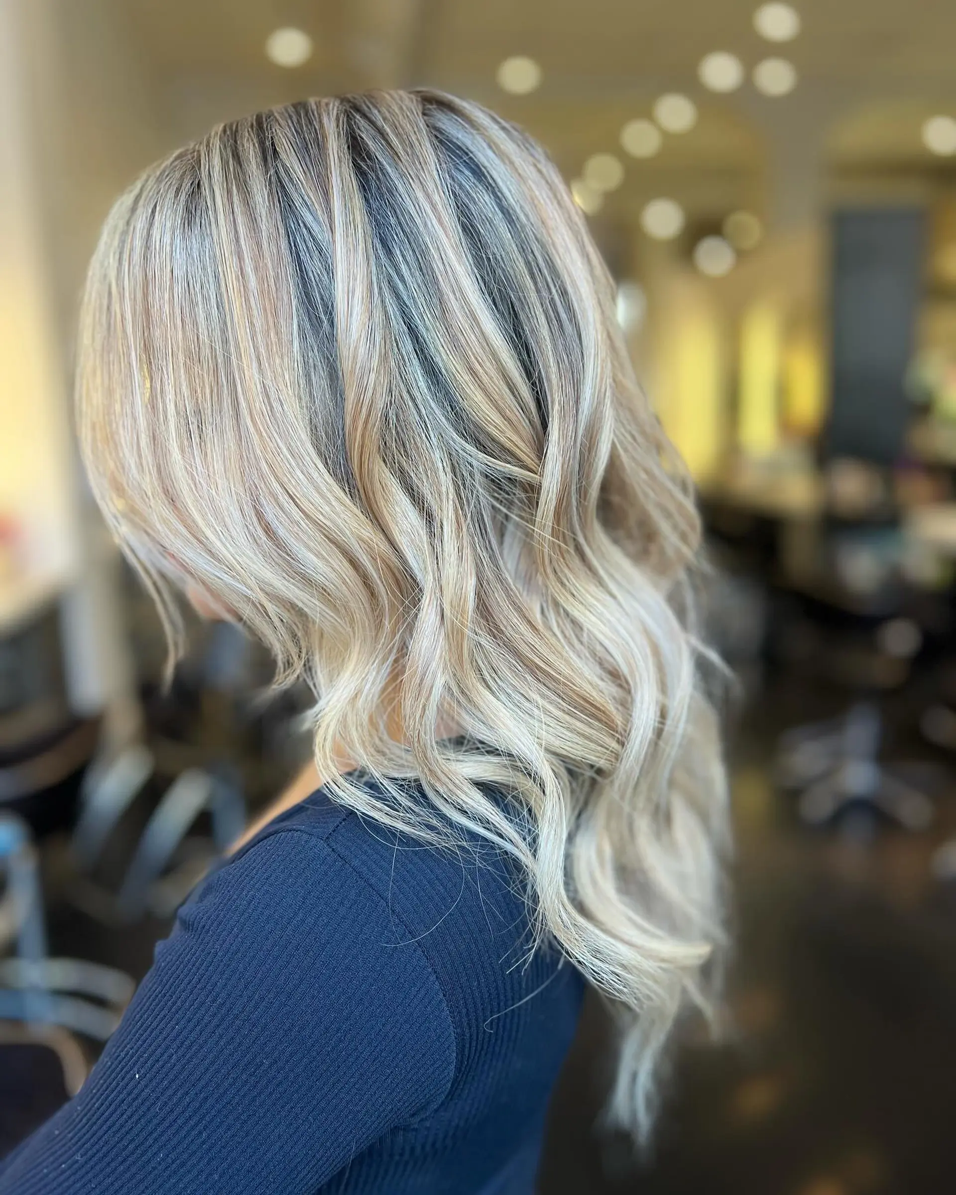 Long dimensional ash blonde hair styled in soft, loose waves with fine foil highlights blended into a natural base. 1