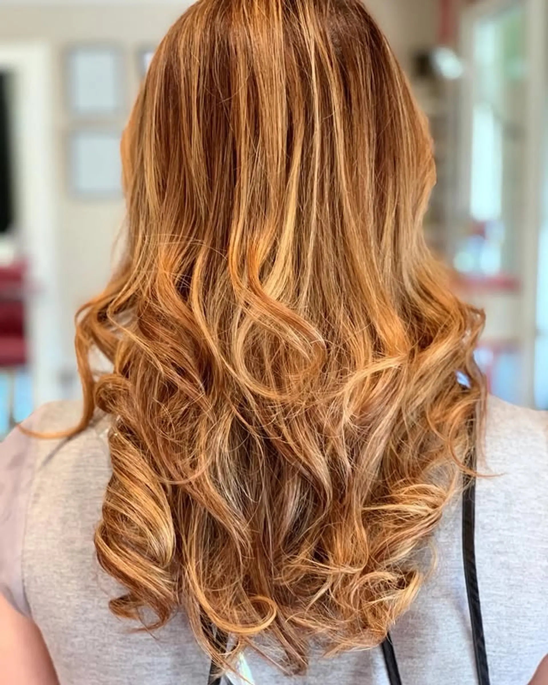Long, wavy hair with voluminous, loose curls, enhanced by a warm honey balayage that blends copper and blonde tones for a dimensional and sun-kissed effect. 1
