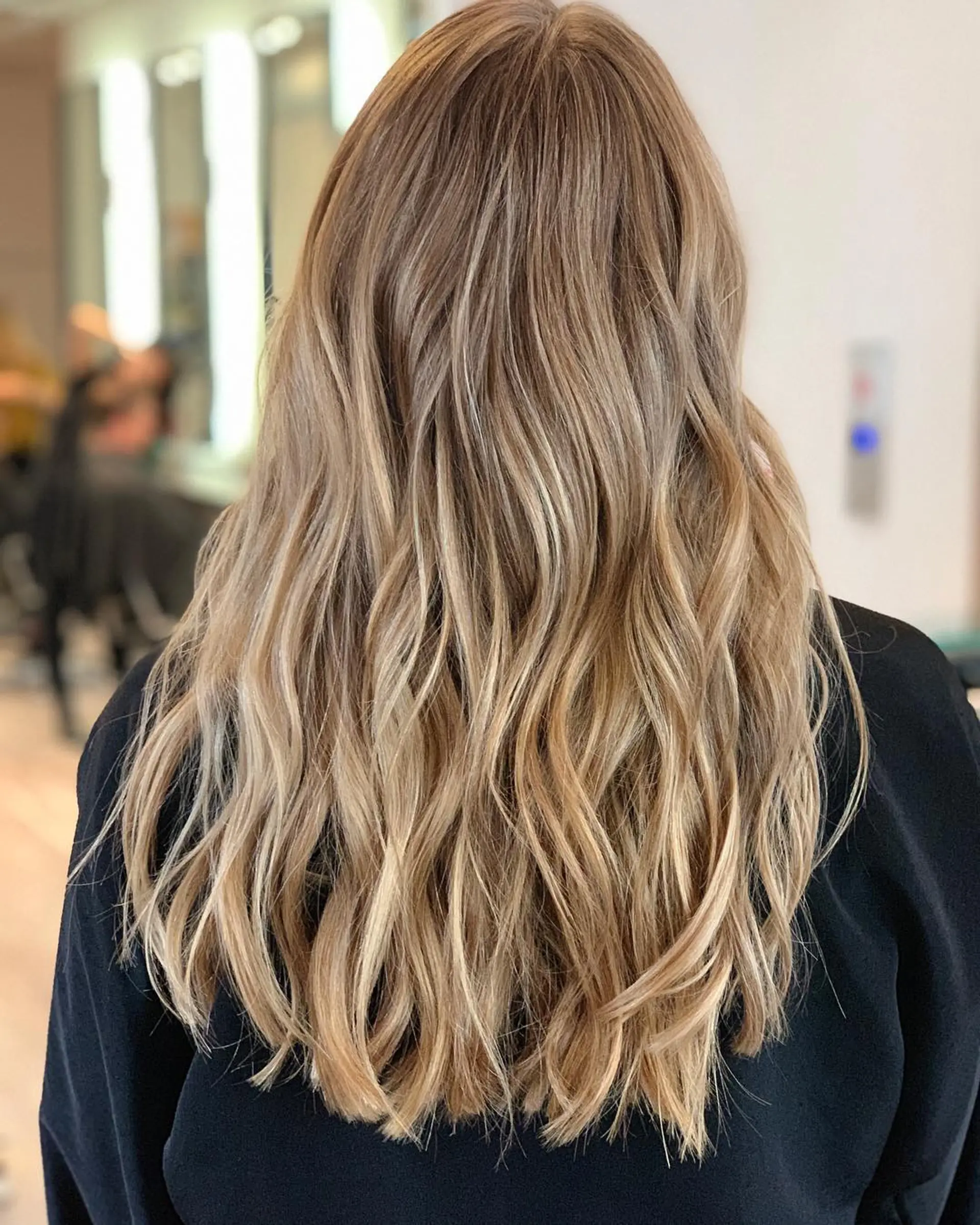 Long, warm blonde hair featuring seamless, fine highlights and styled into loose, effortless waves. 1