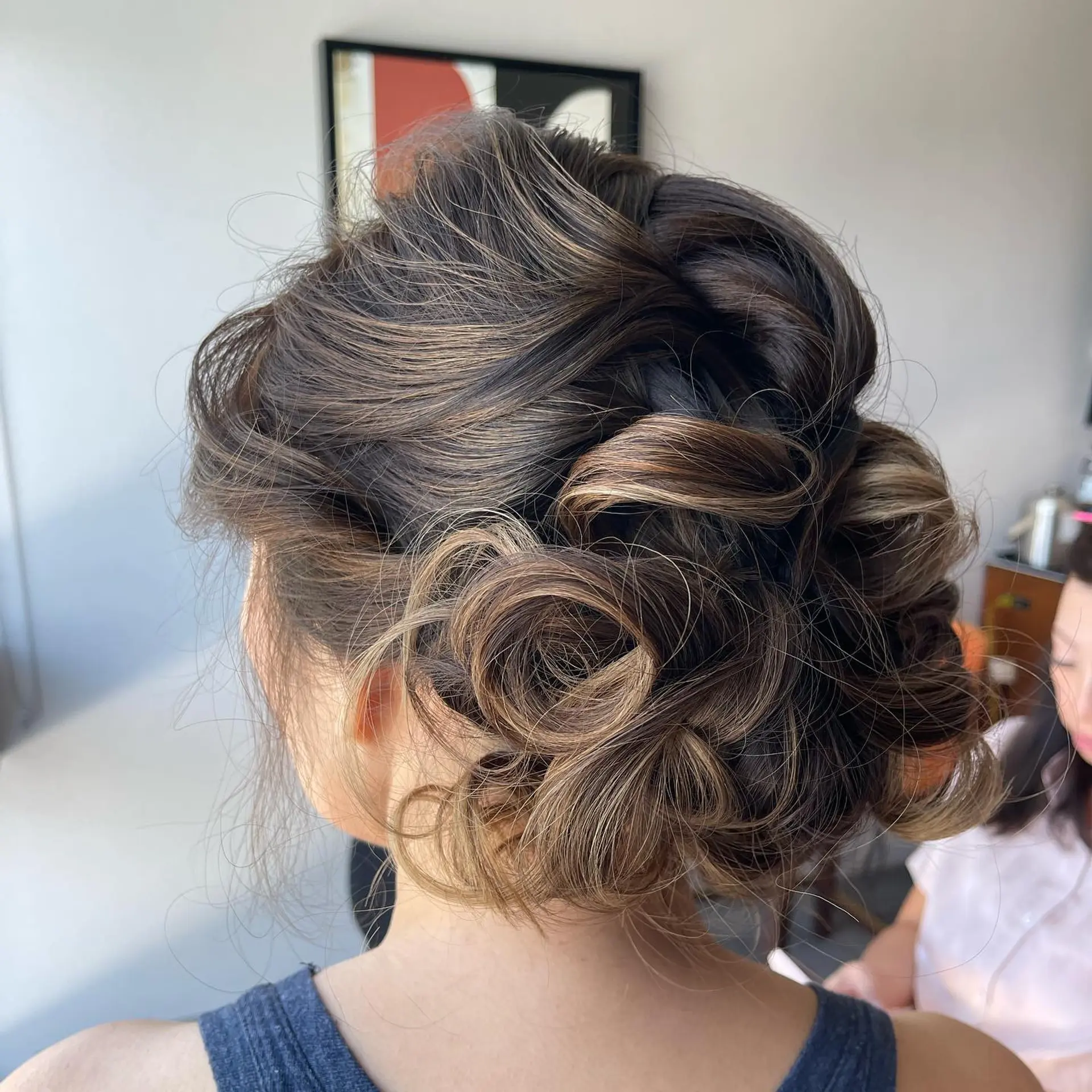 A romantic low bun updo featuring curled, intertwined strands with volume at the crown and textured detailing throughout. 1