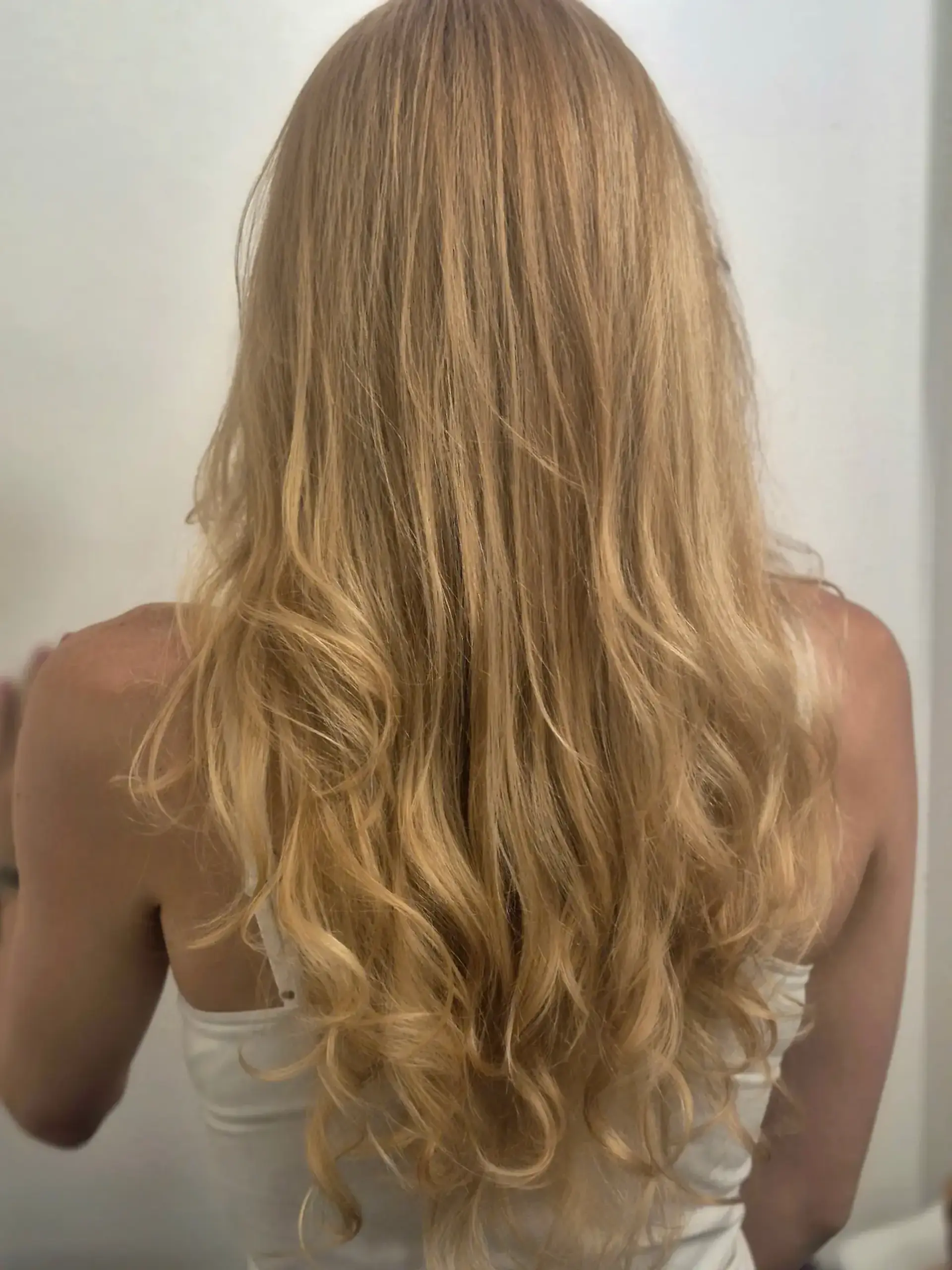 Long warm golden blonde highlighted hair styled into soft loose waves towards the ends. 1