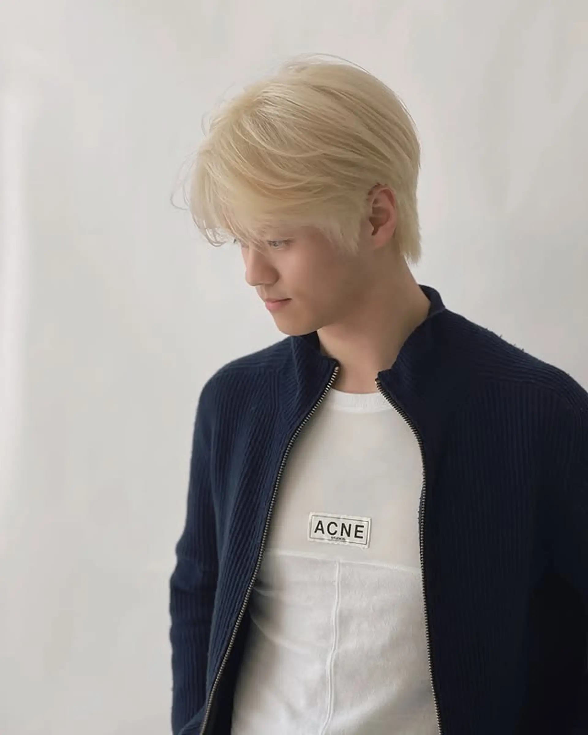 A medium length, icy blonde Korean wave hairstyle with a slight side part and textured finish. 1