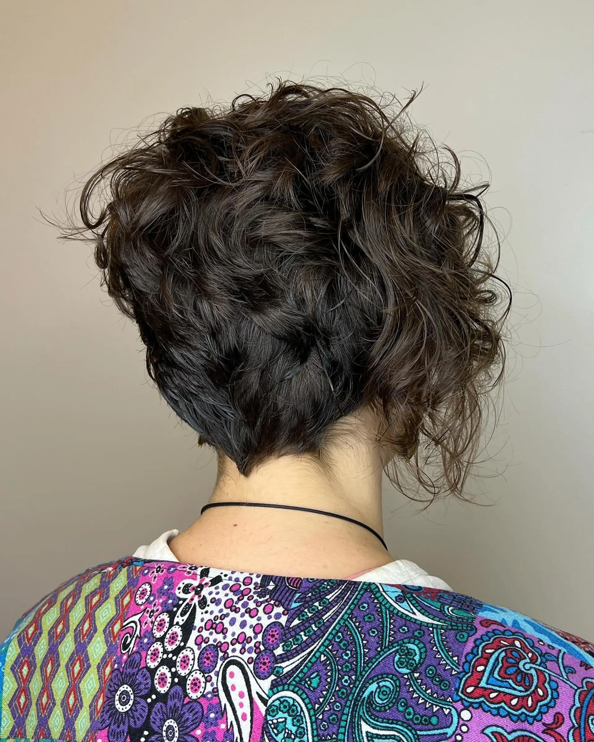 A textured asymmetrical curly pixie cut featuring a tapered V-shaped nape and voluminous, tousled curls. 1