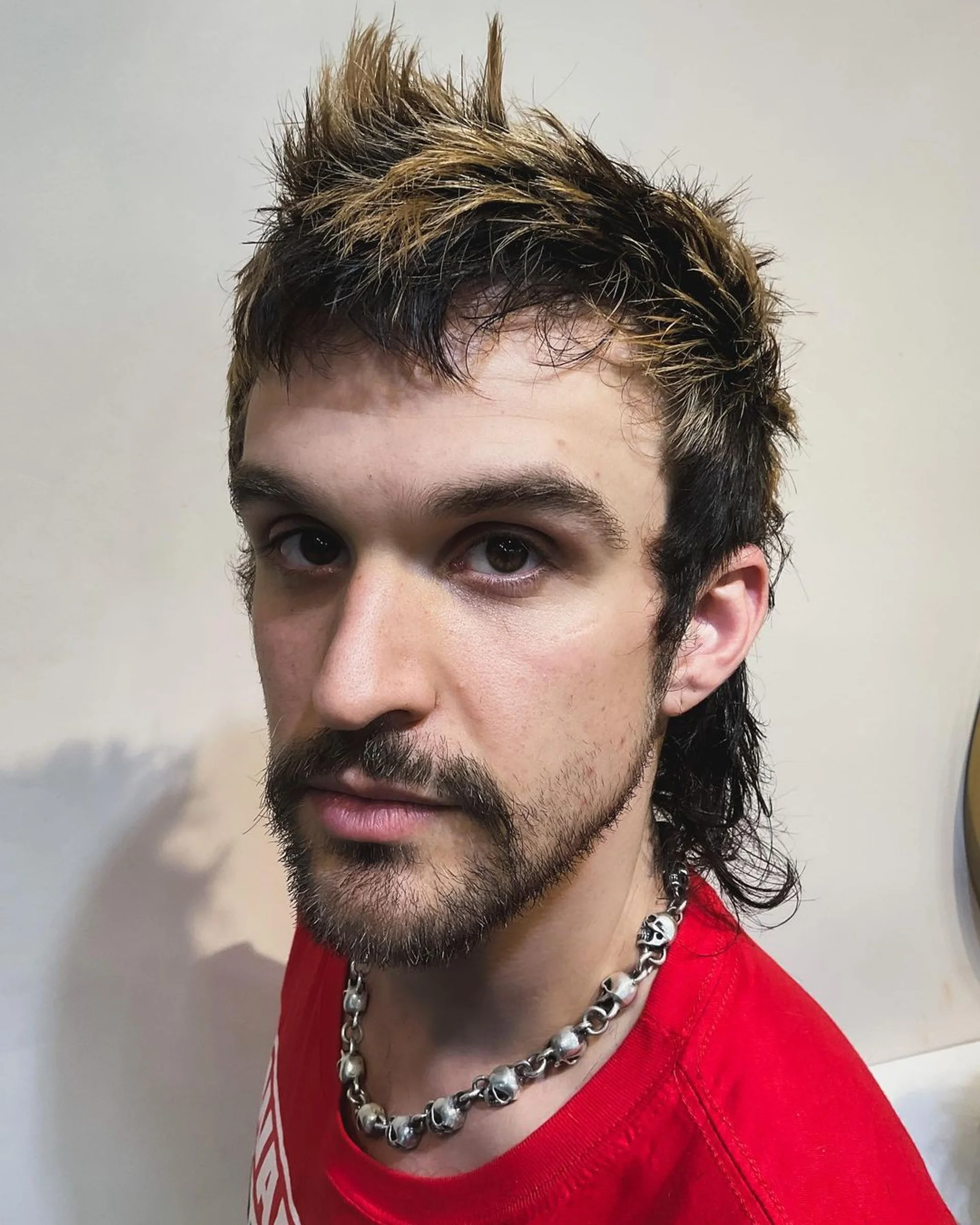 A model with a blended mullet featuring a spiky dark brown top with blonde highlights, showcasing one of NYC's top anti-trend hairstyles for 2025. - Preview 1