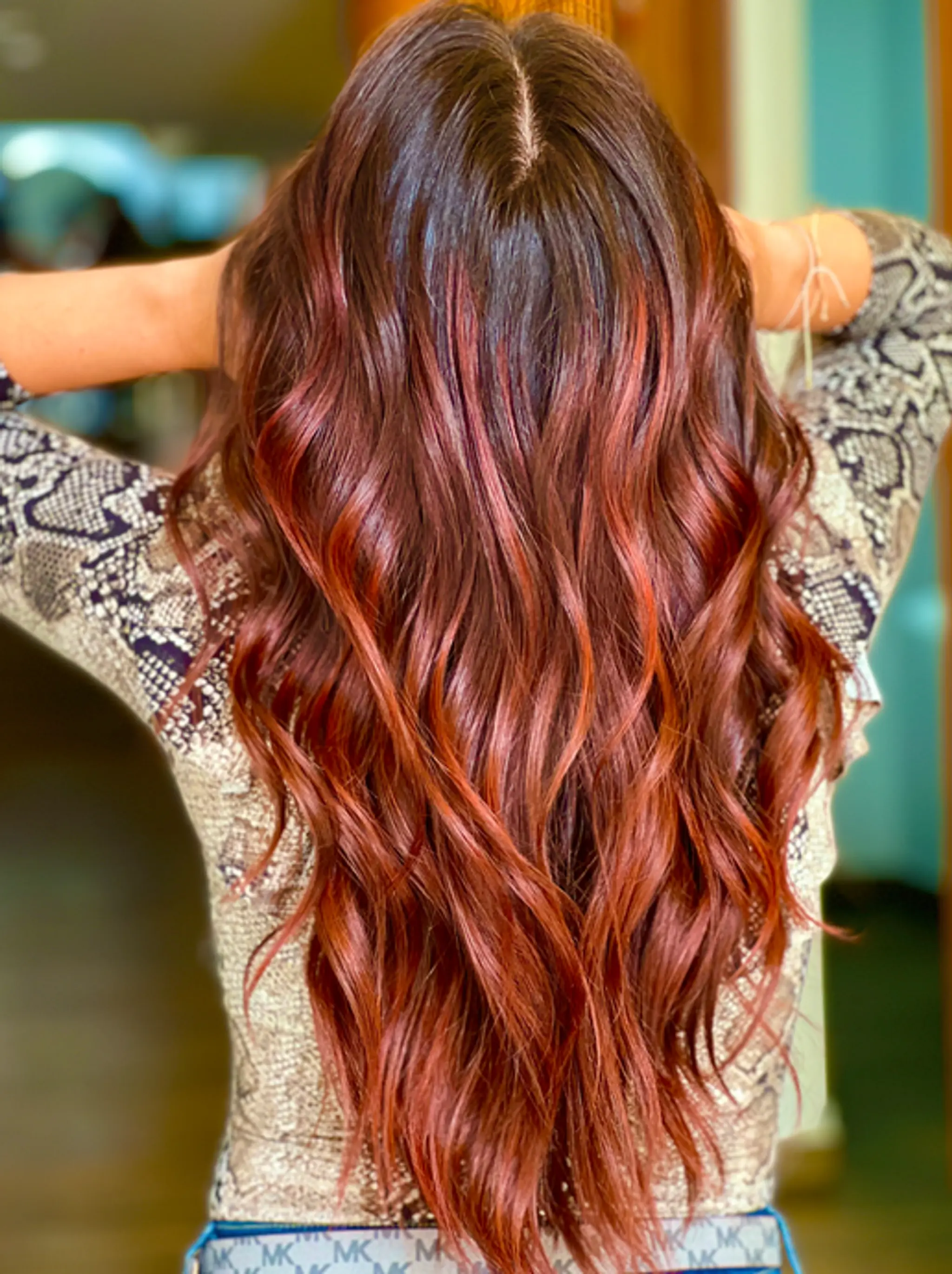 Very long, wavy hair with dark brown and copper red balayage. Features loose waves and a voluminous, shiny finish.