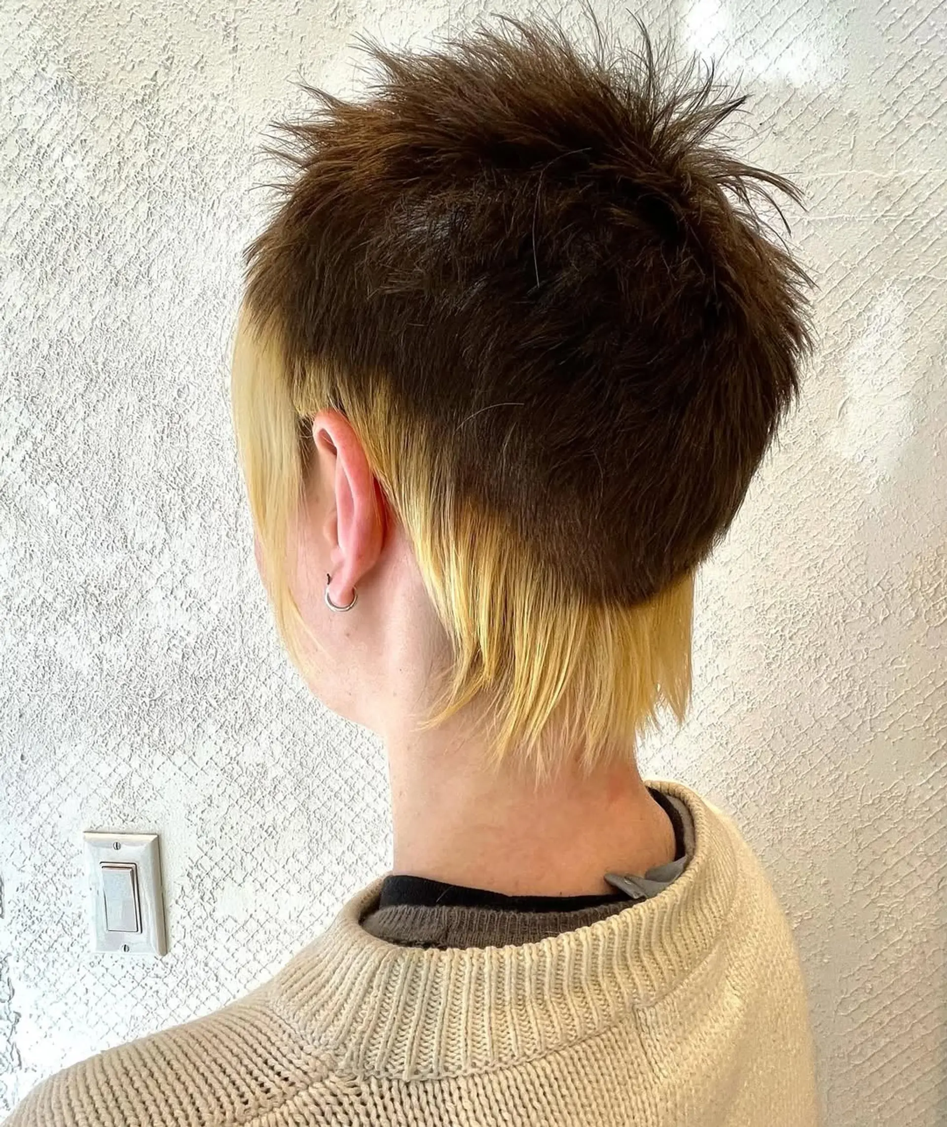 A short, choppy mullet with a blonde and dark brown contrast. The hairstyle features an undercut, a textured top, and an ear-length fringe with straight, layered strands for a spiky look. 3
