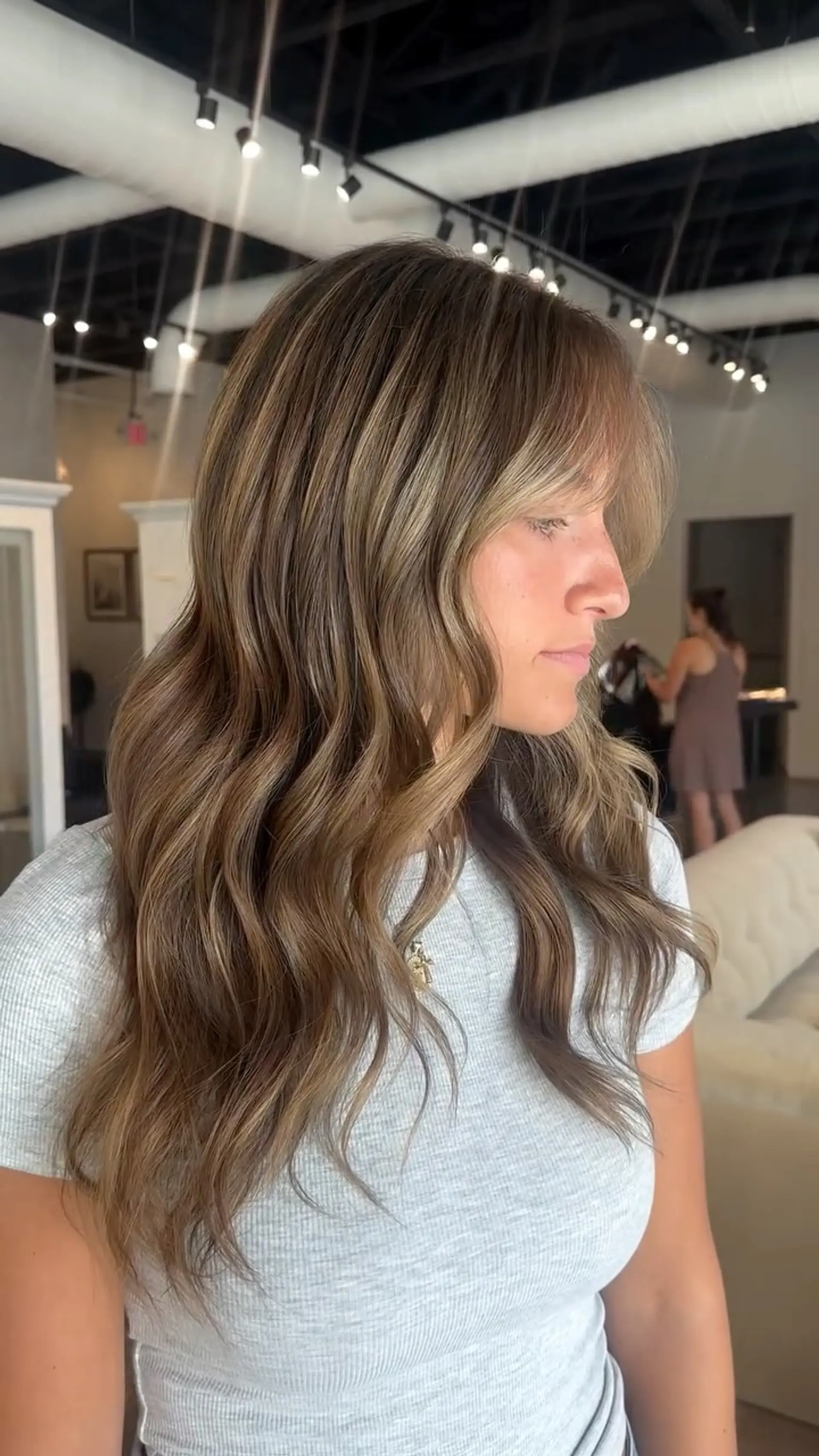 Long dimensional bronde hair styled with loose soft waves and wispy face-framing bangs. 1