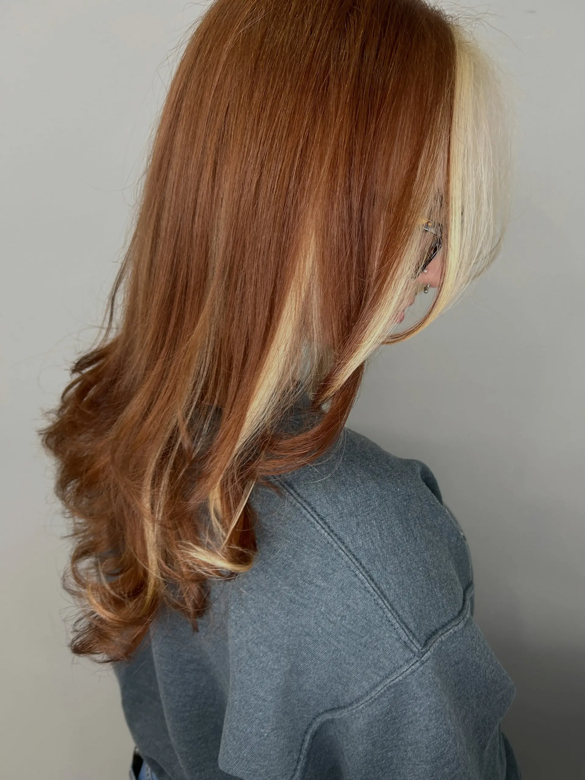 A rich copper-auburn style accented by high-contrast blonde face-framing and peekaboo highlights, styled with soft outward curls at the ends. 1