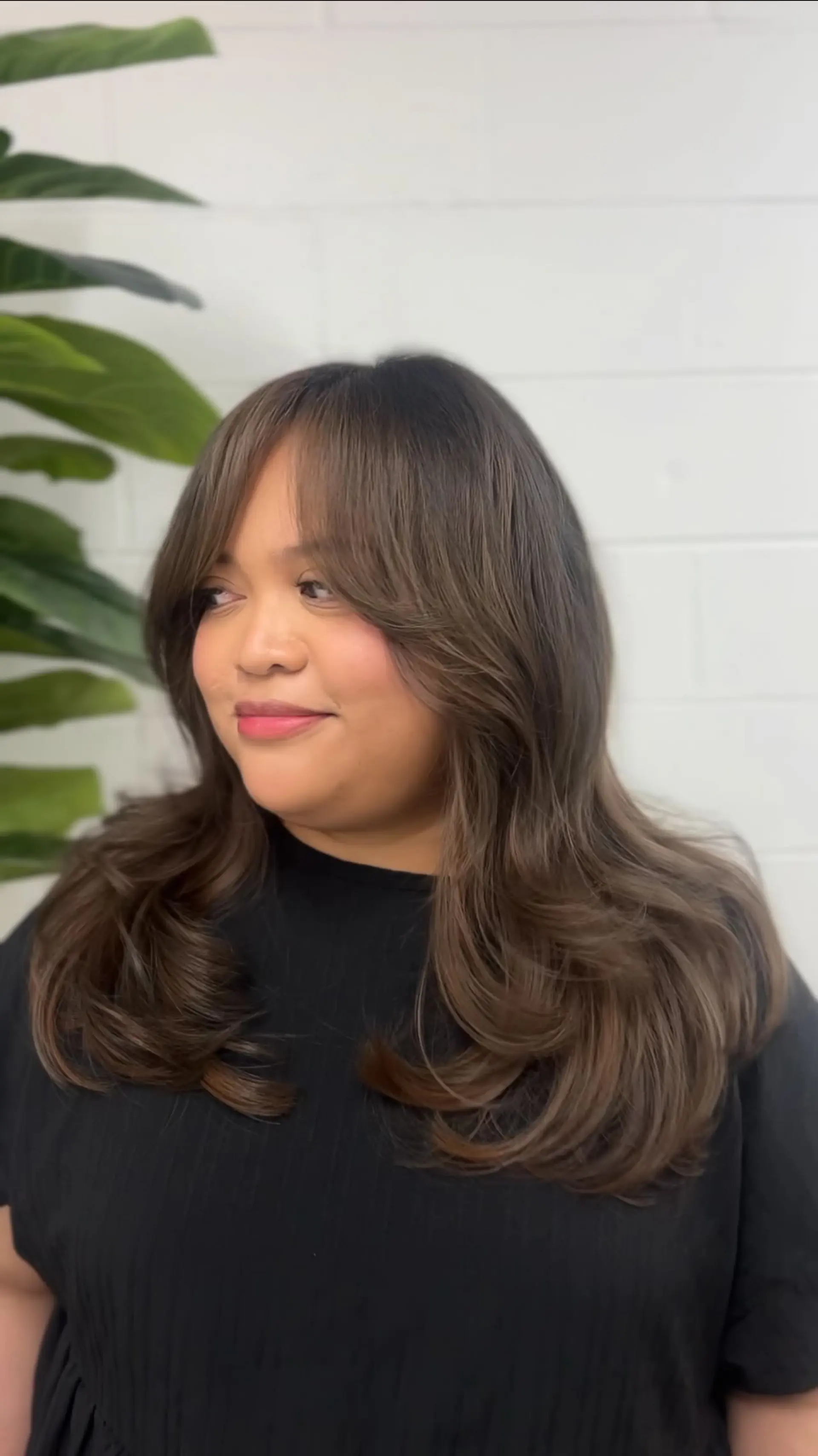 Voluminous long layered haircut in rich dimensional brunette, styled with curled-under ends and soft curtain bangs. 1