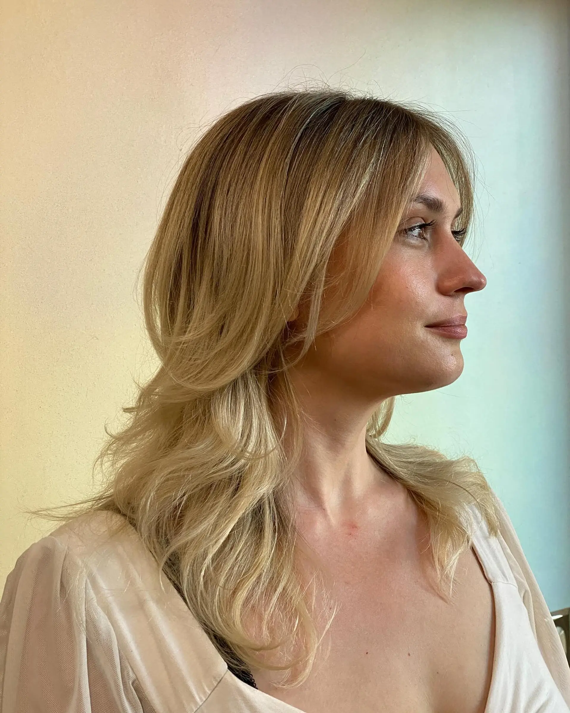 Medium-length layered golden blonde hair styled in soft waves with face-framing curtain bangs and a blended root tap. 1