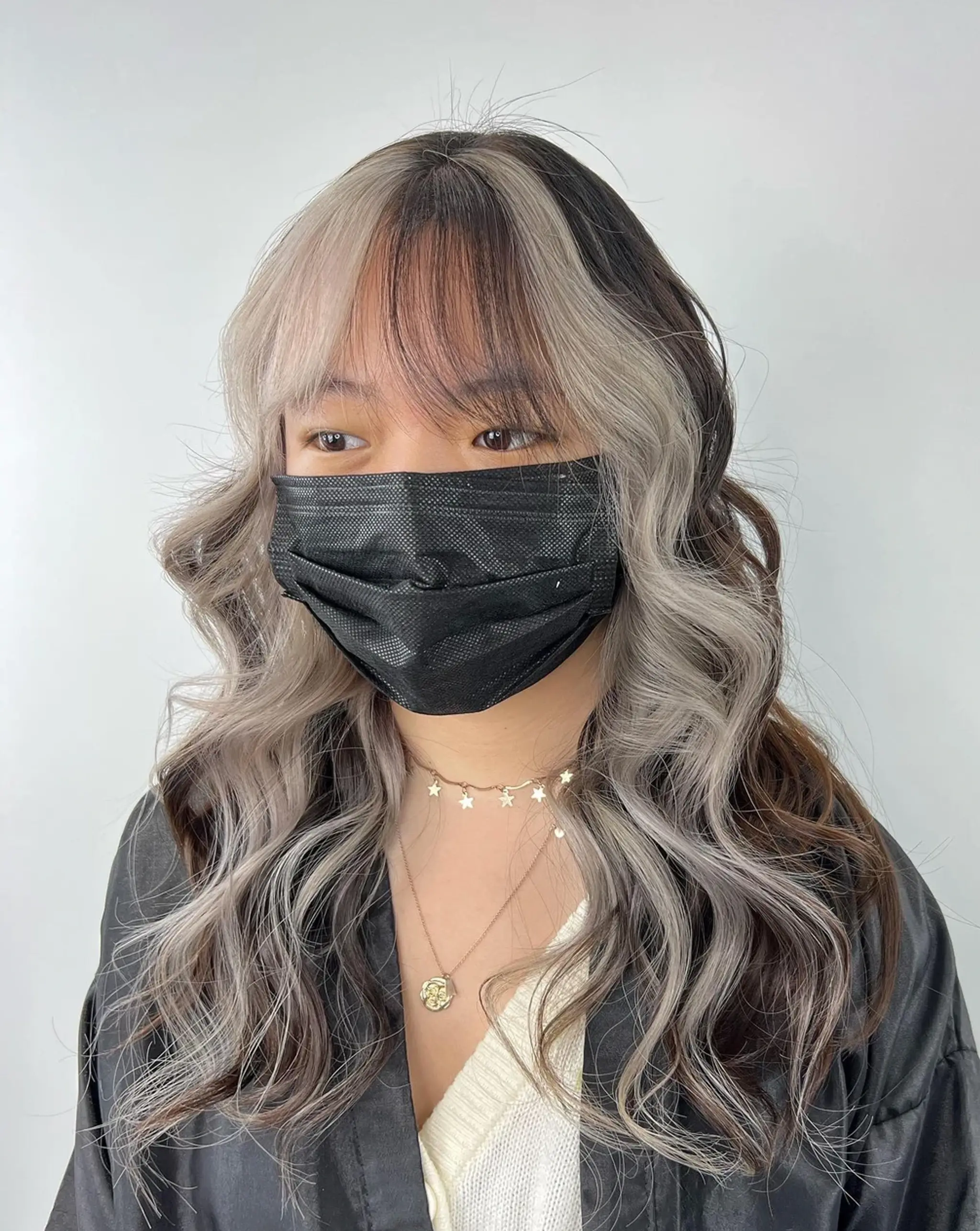 Long, voluminous waves with black shadow roots and silvery highlighted ends, featuring curtain bangs for added texture and style. 